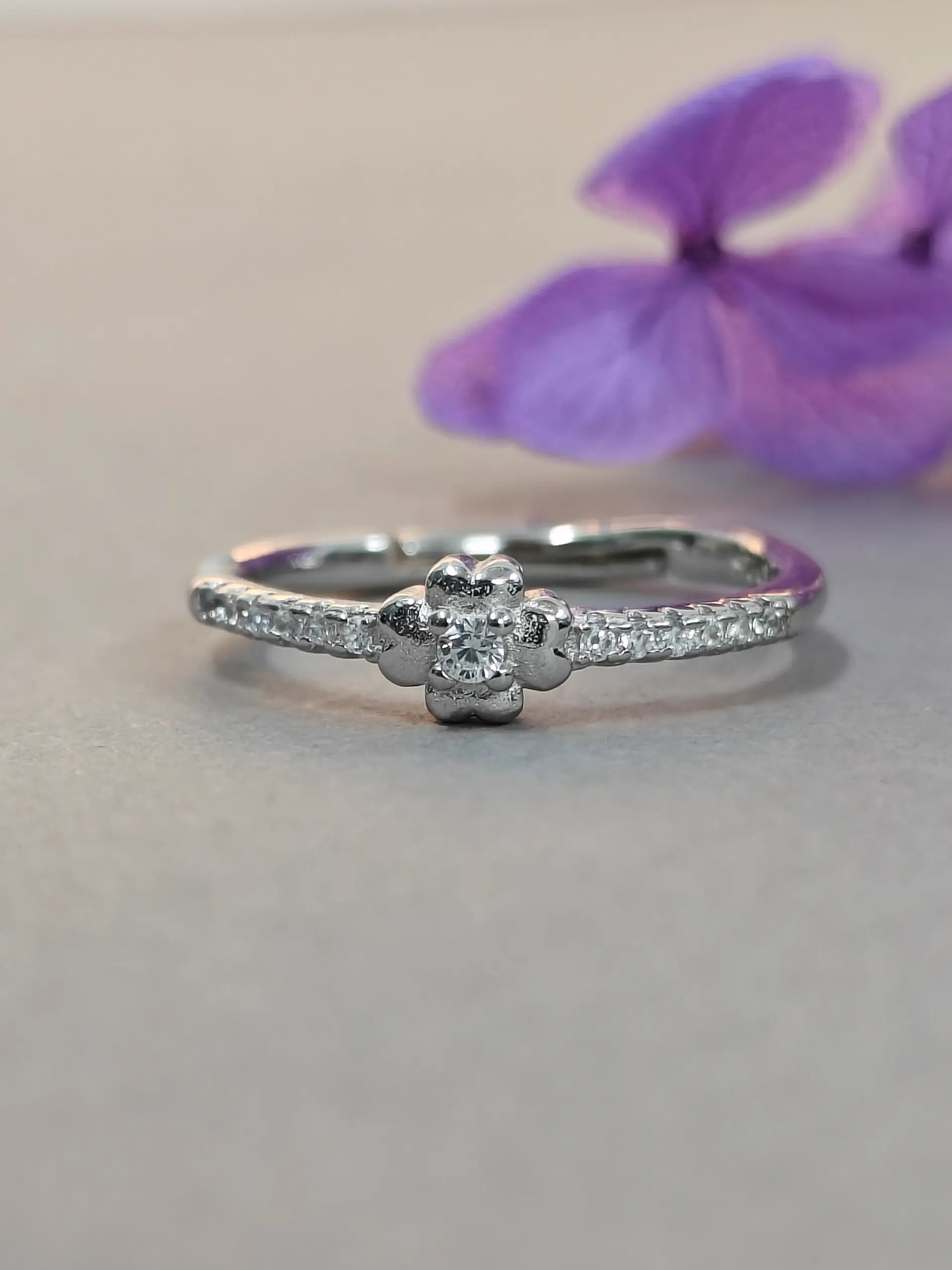 Silver ring with small diamonds on a light gray background with purple flowers.