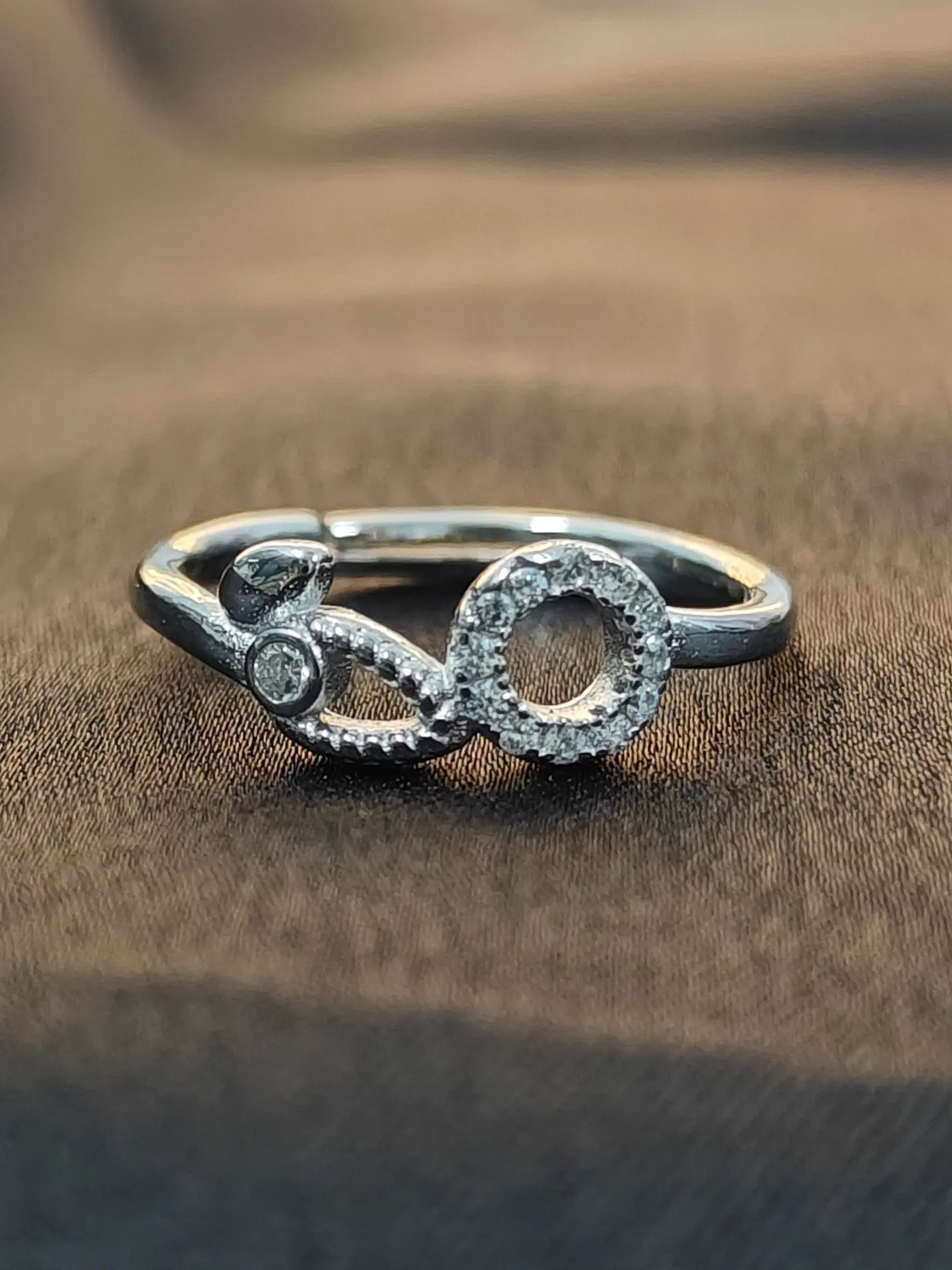 Silver ring with intricate design on a brown fabric background