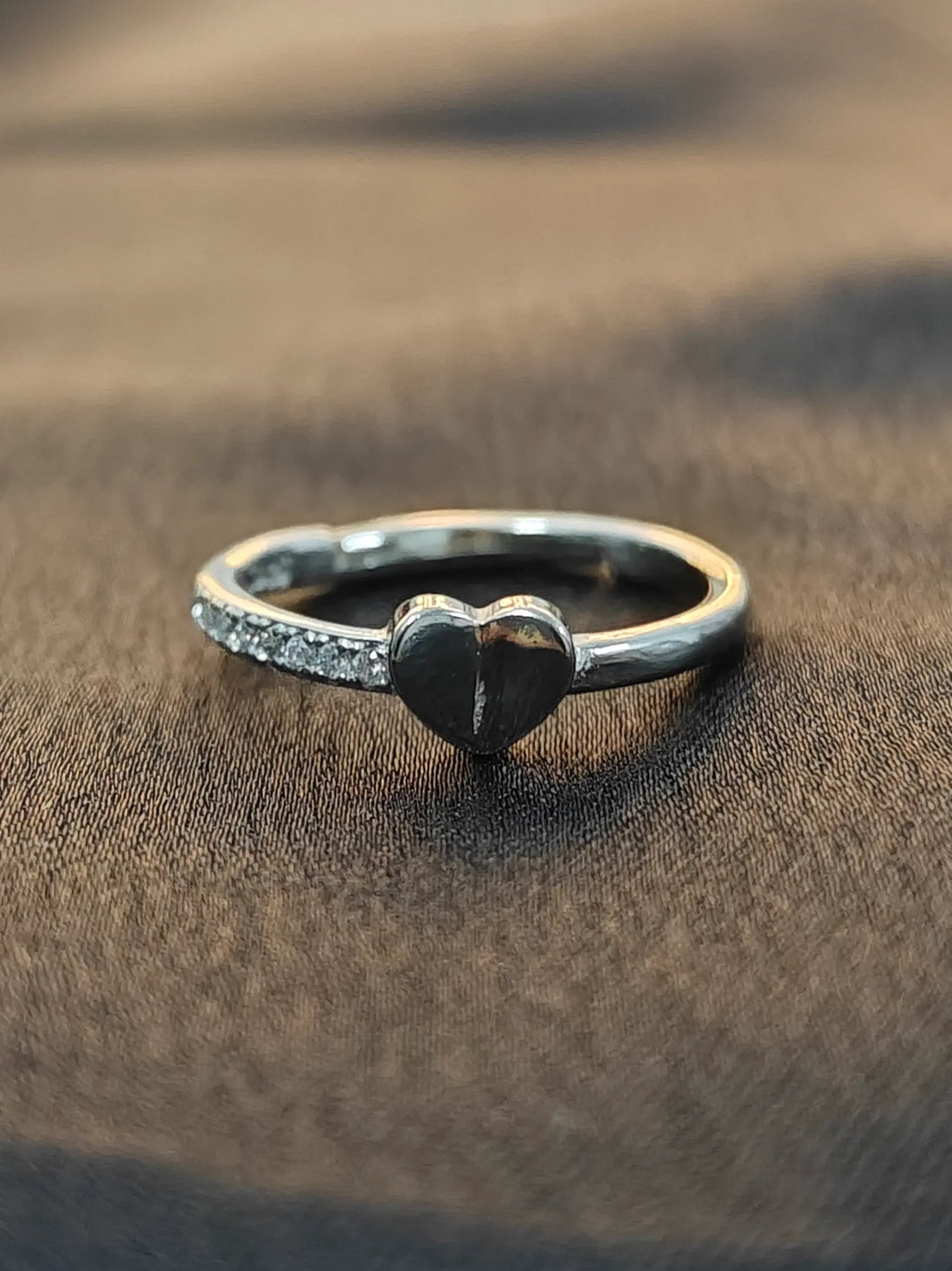 Silver ring with a heart-shaped design on a brown fabric background