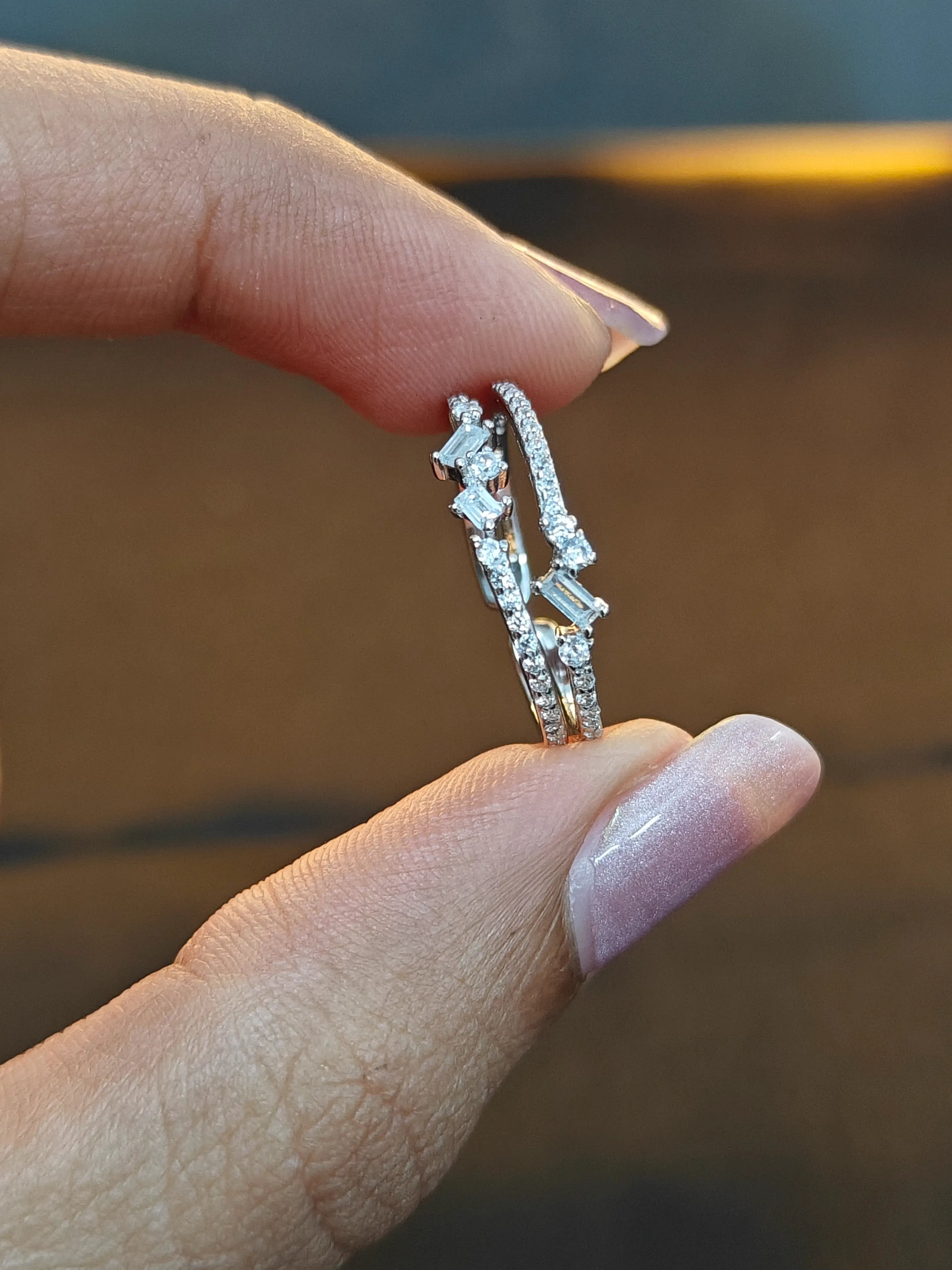 Silver ring with gemstones held between fingers against a blurred background