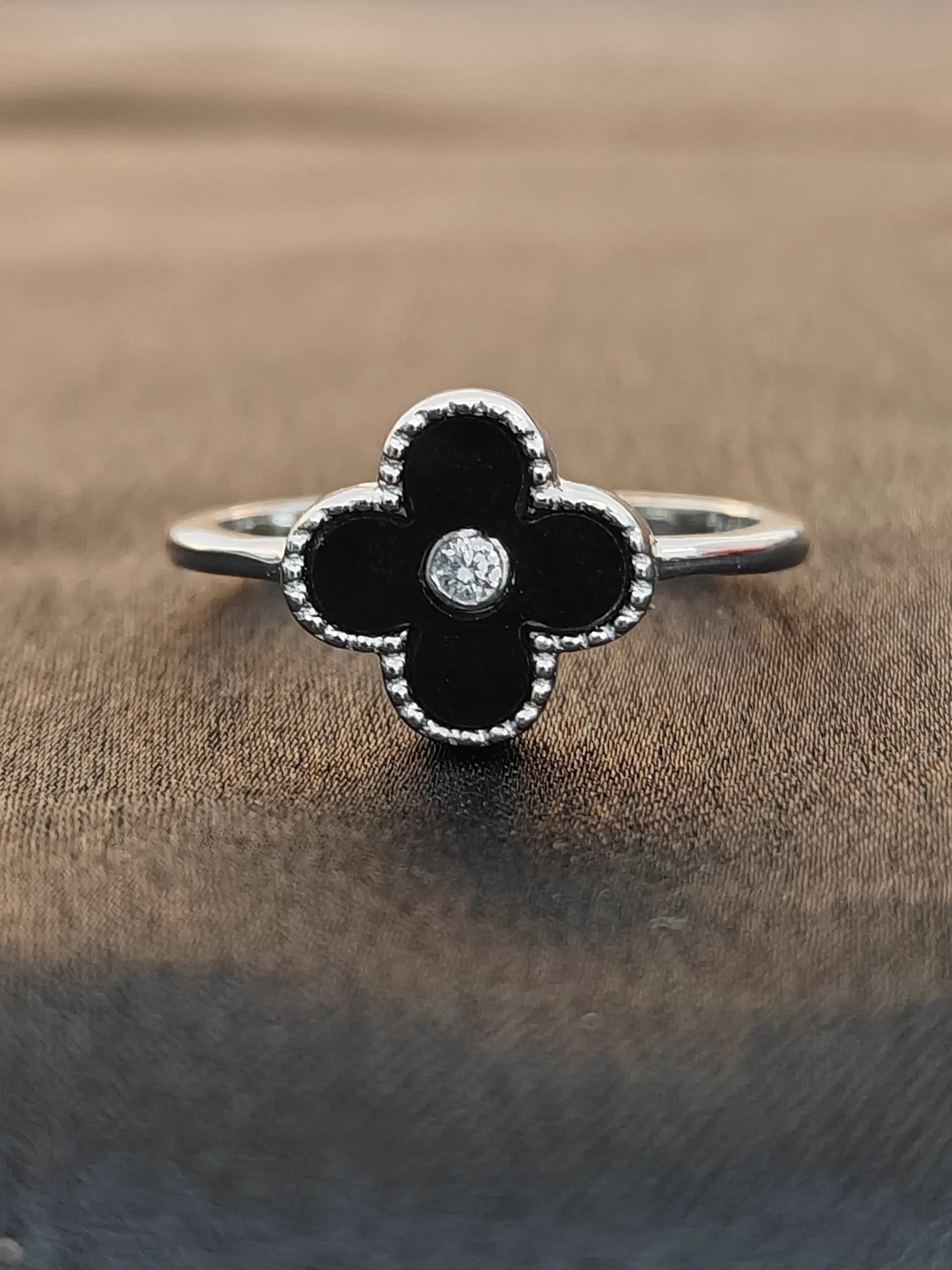Black flower-shaped ring with a diamond on a brown fabric background