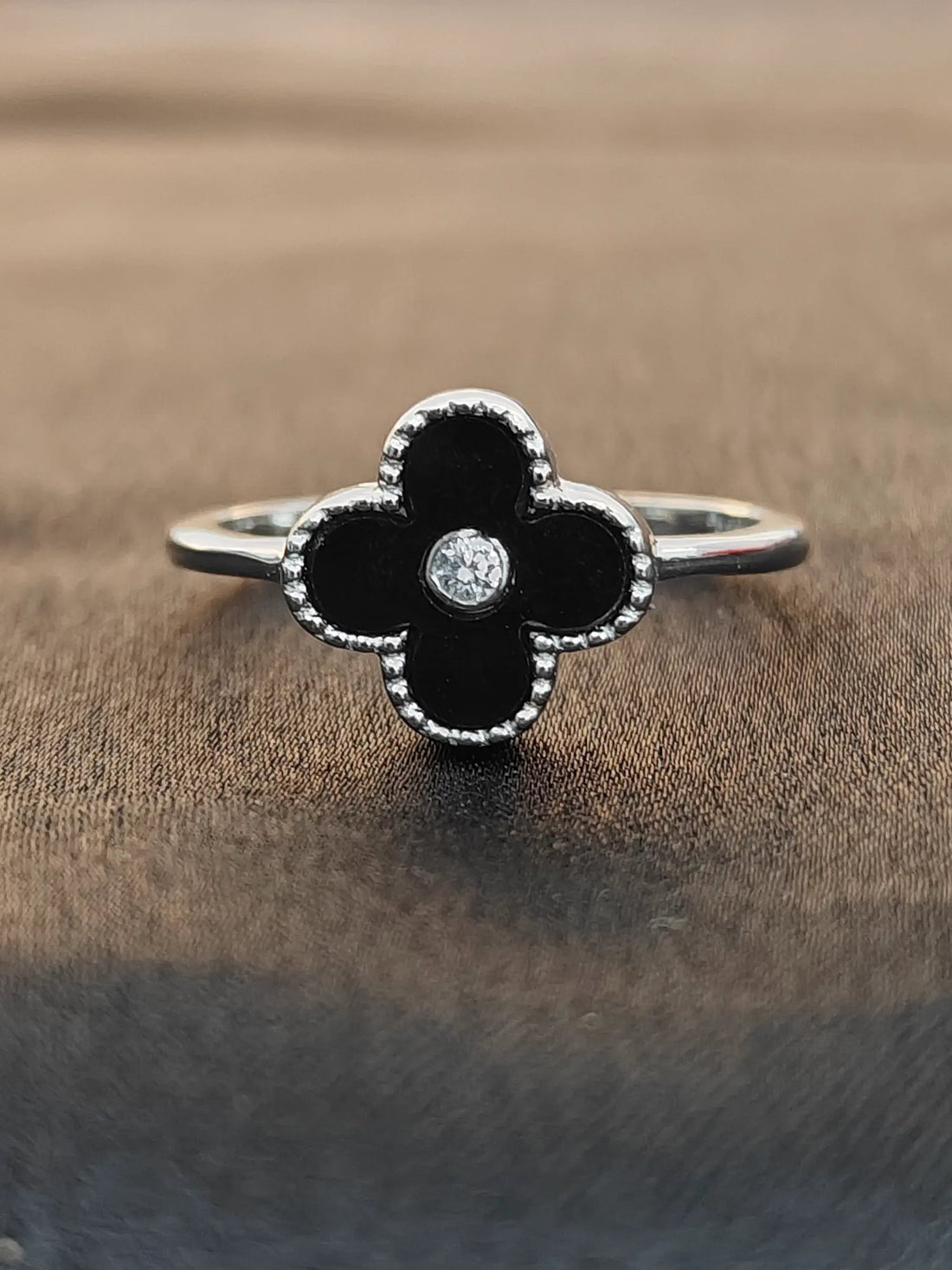 Black flower-shaped ring with a diamond on a brown fabric background