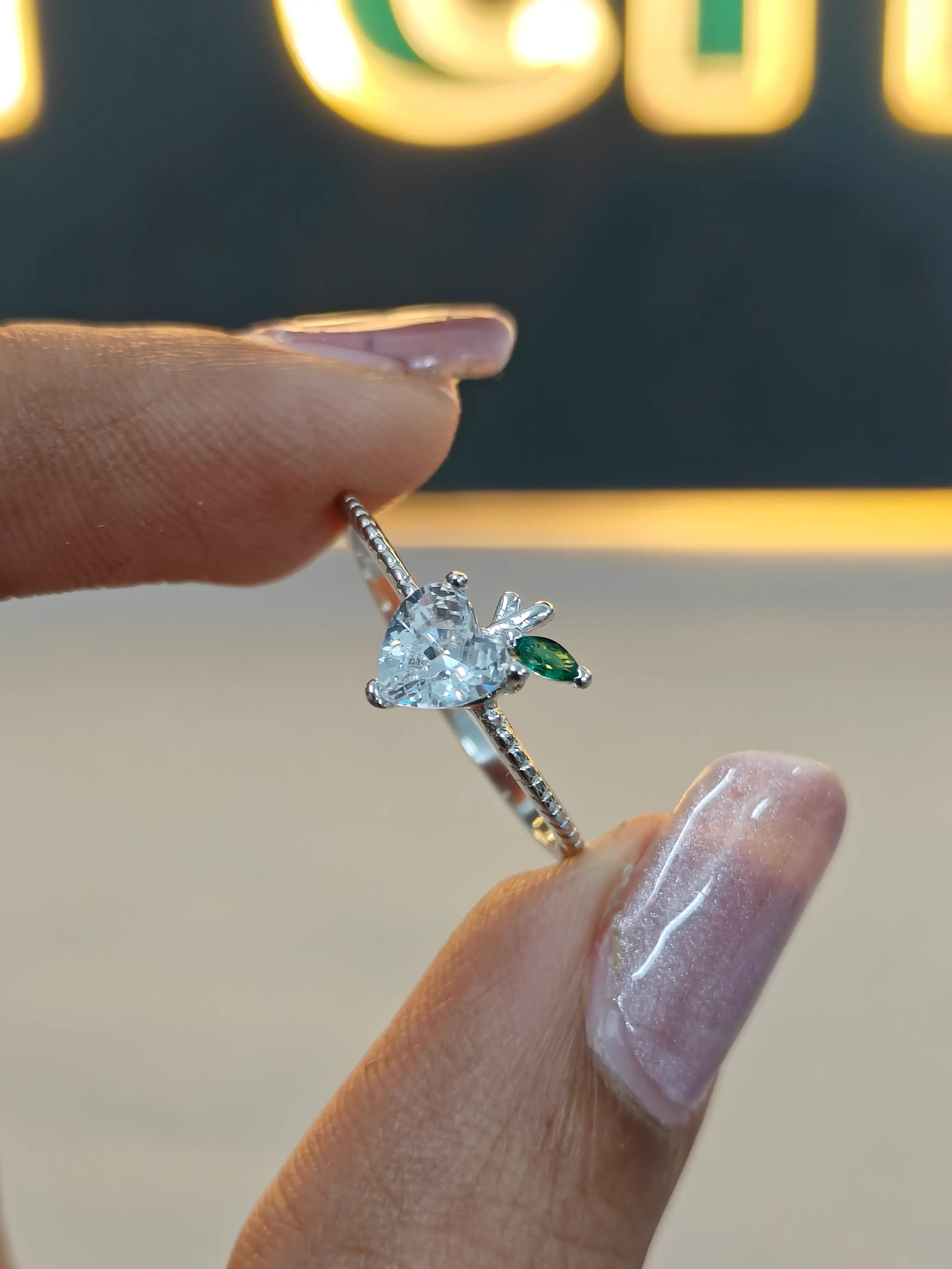 Silver ring with a heart-shaped diamond held by a hand against a blurred background