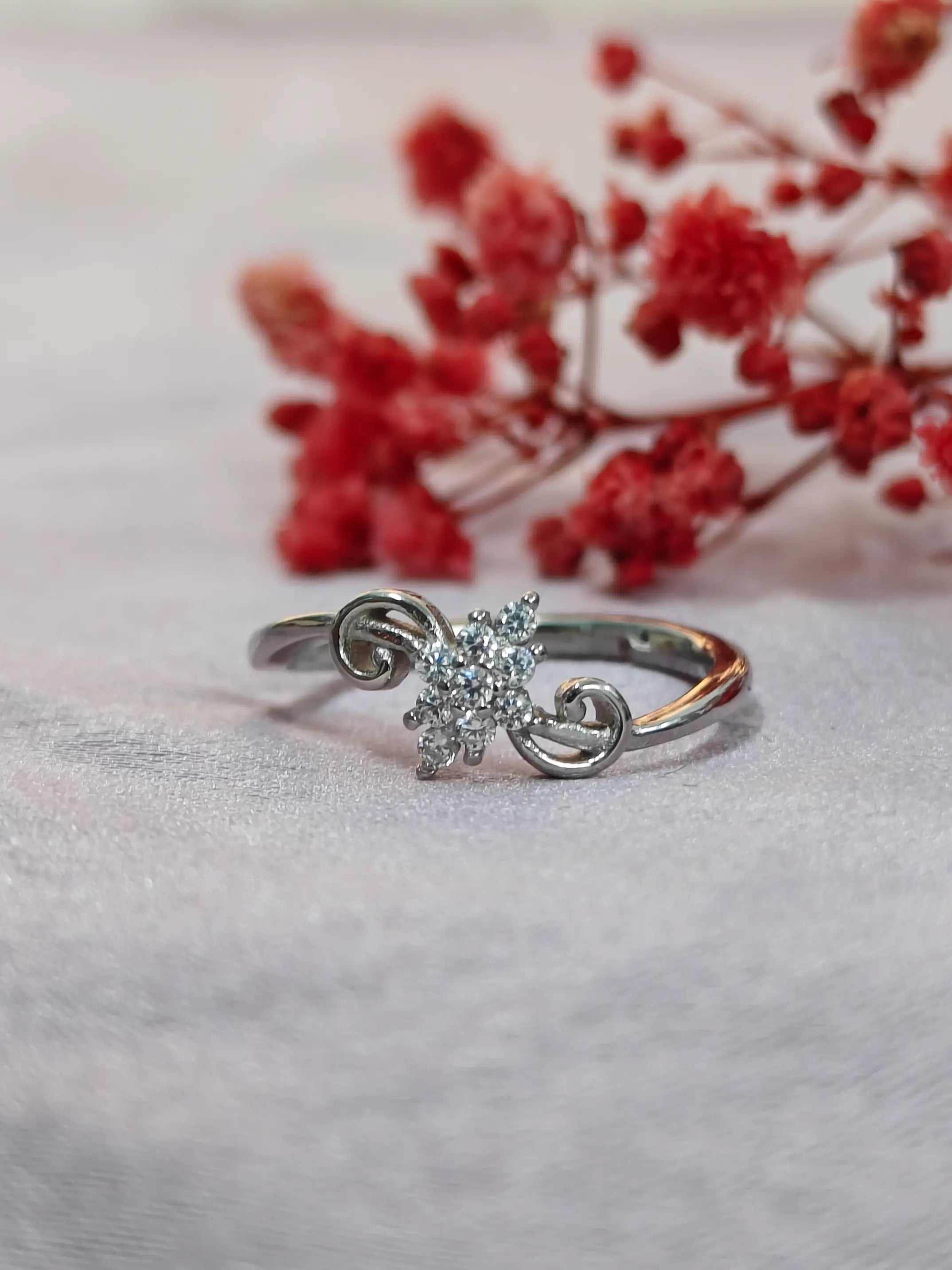 Silver ring with a diamond on a light background with red flowers