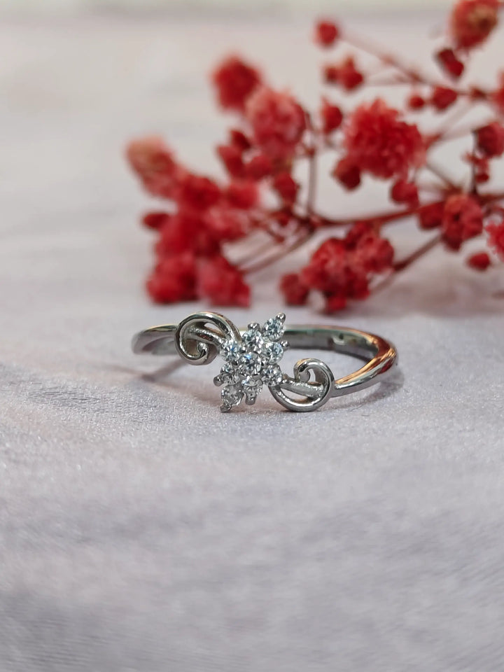 Silver ring with a diamond on a light background with red flowers