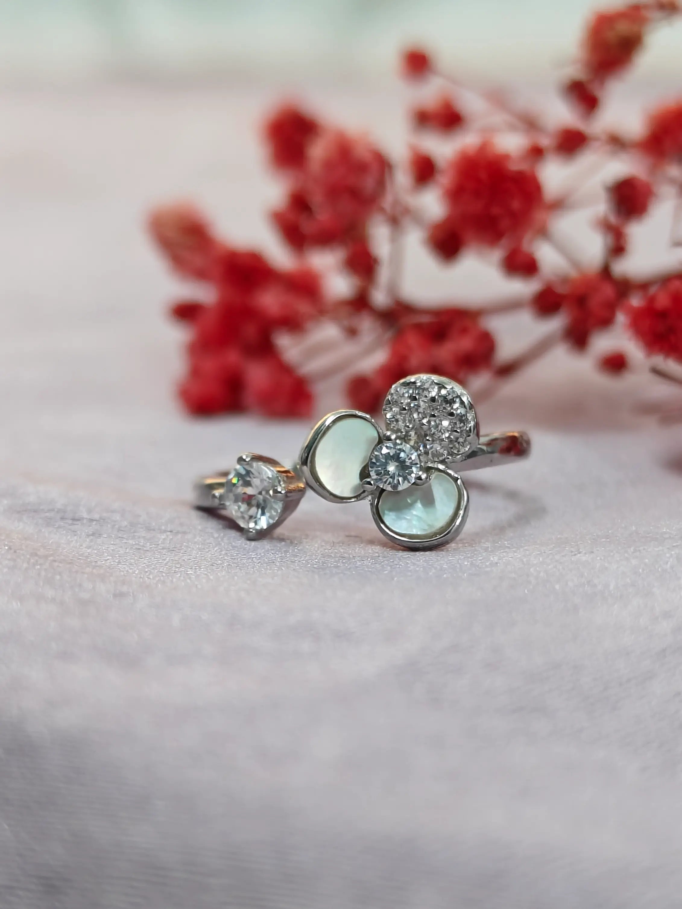 Two silver rings with gemstones on a soft pink surface with red flowers in the background