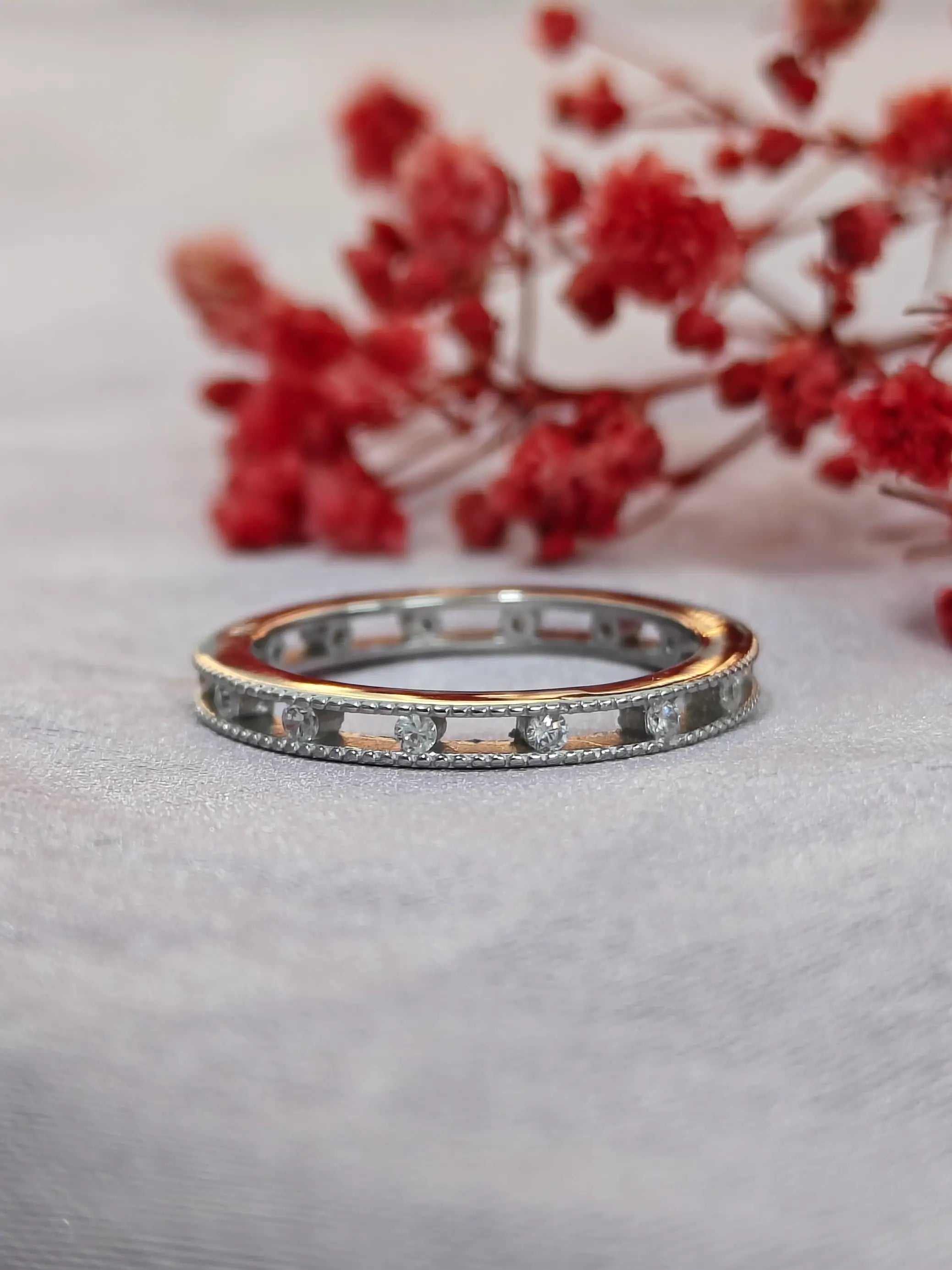 Two diamond rings on a gray surface with red floral decorations in the background