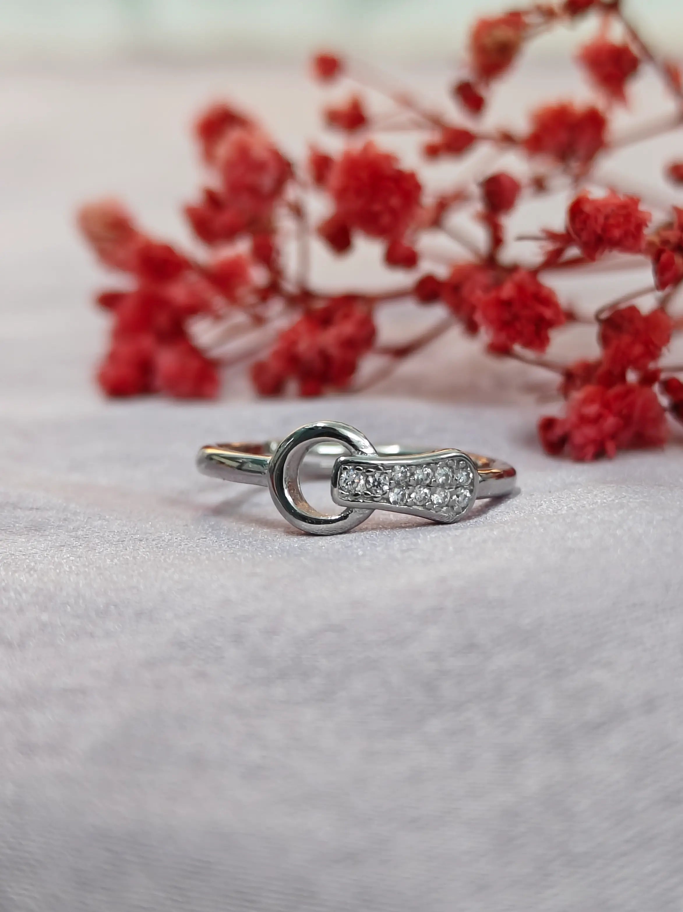 Silver ring with small diamonds on a light gray surface with red flowers in the background