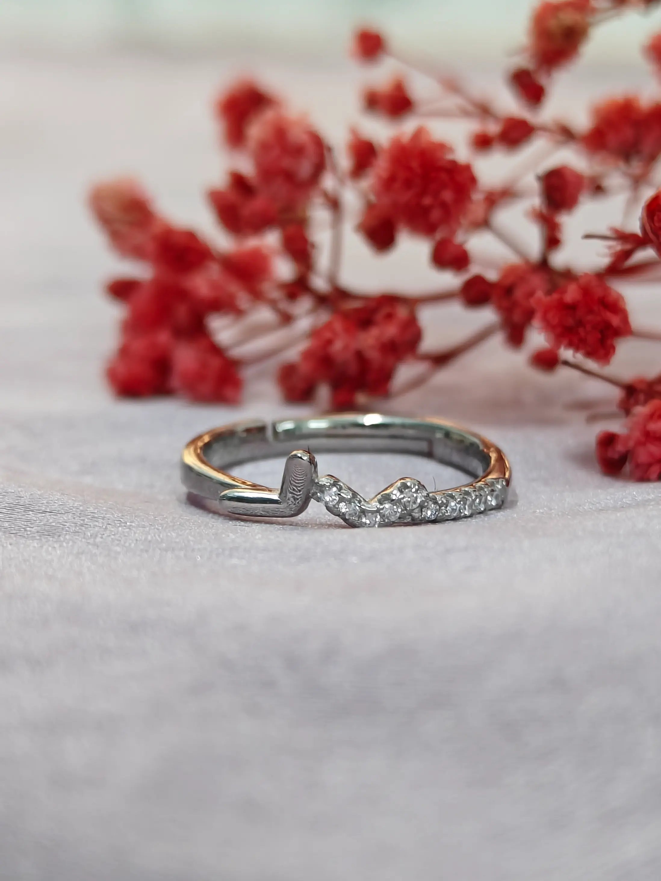 Silver ring with a small diamond on a light gray surface with red flowers in the background