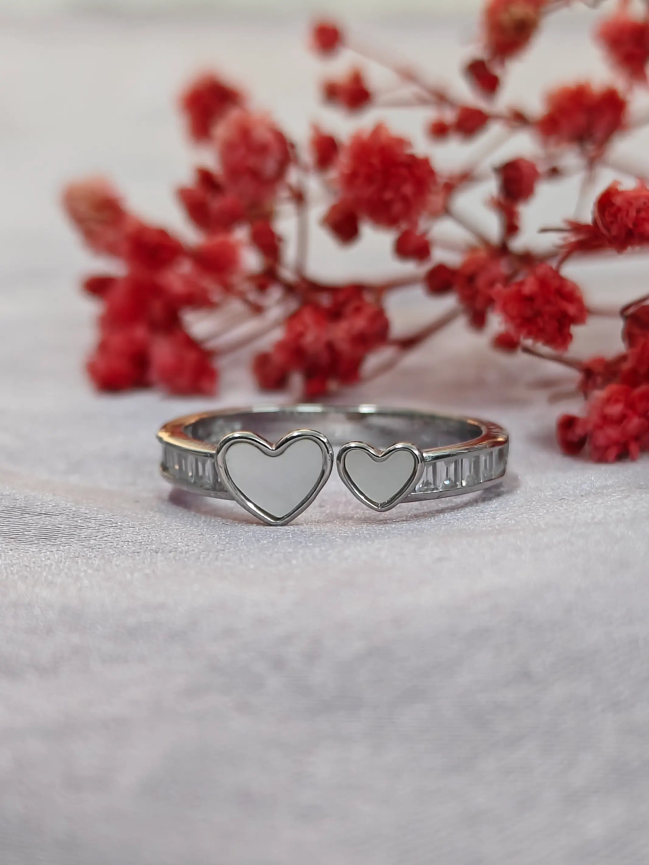 Silver ring with heart designs on a light background with red flowers.