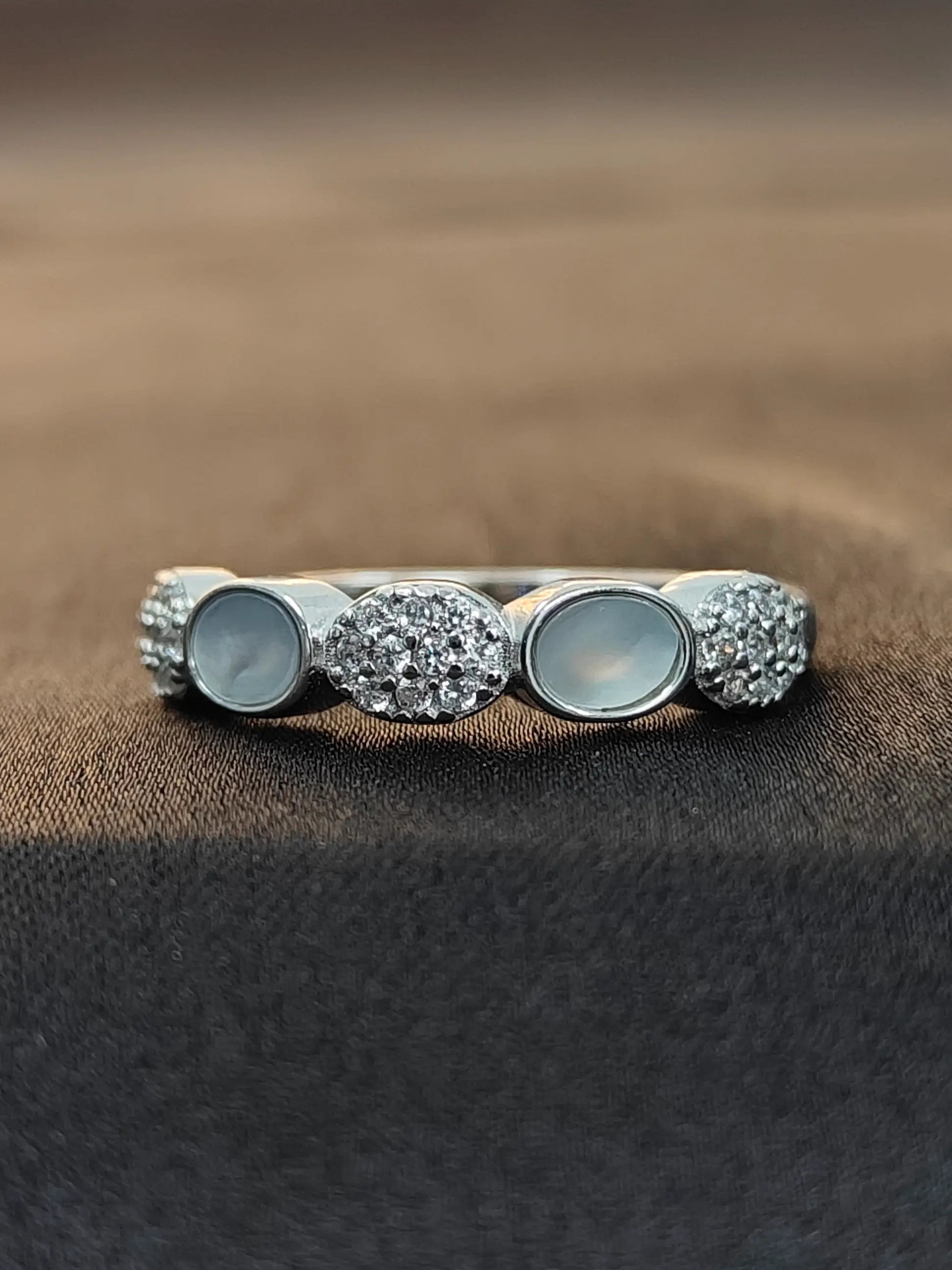 Silver ring with circular gemstones on a brown fabric background