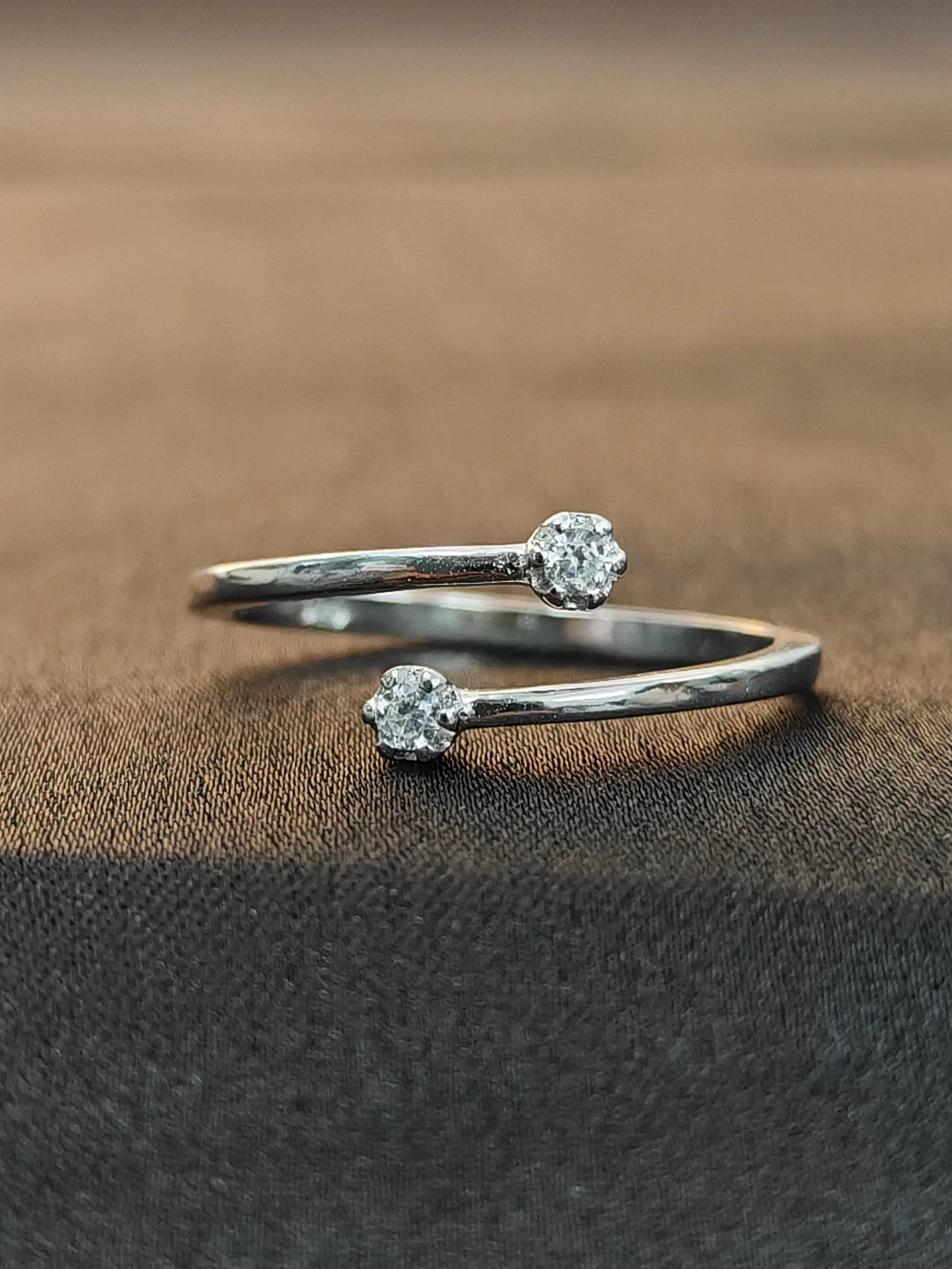 Silver open ring with diamond-like stones on a brown fabric background