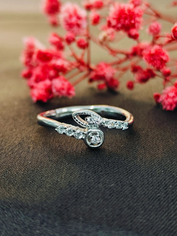 Silver ring with a diamond on a dark fabric background with red flowers.