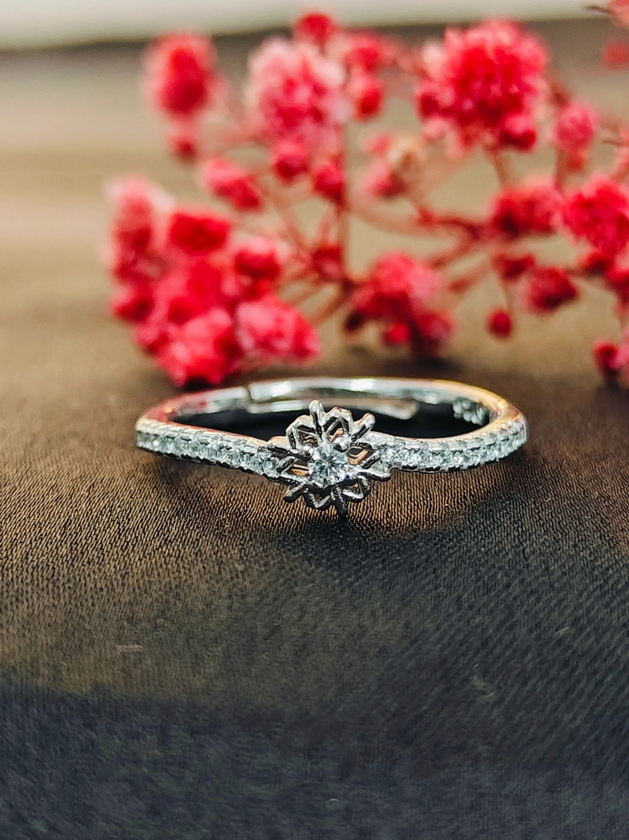 Silver ring with a diamond on a brown fabric background with red flowers.