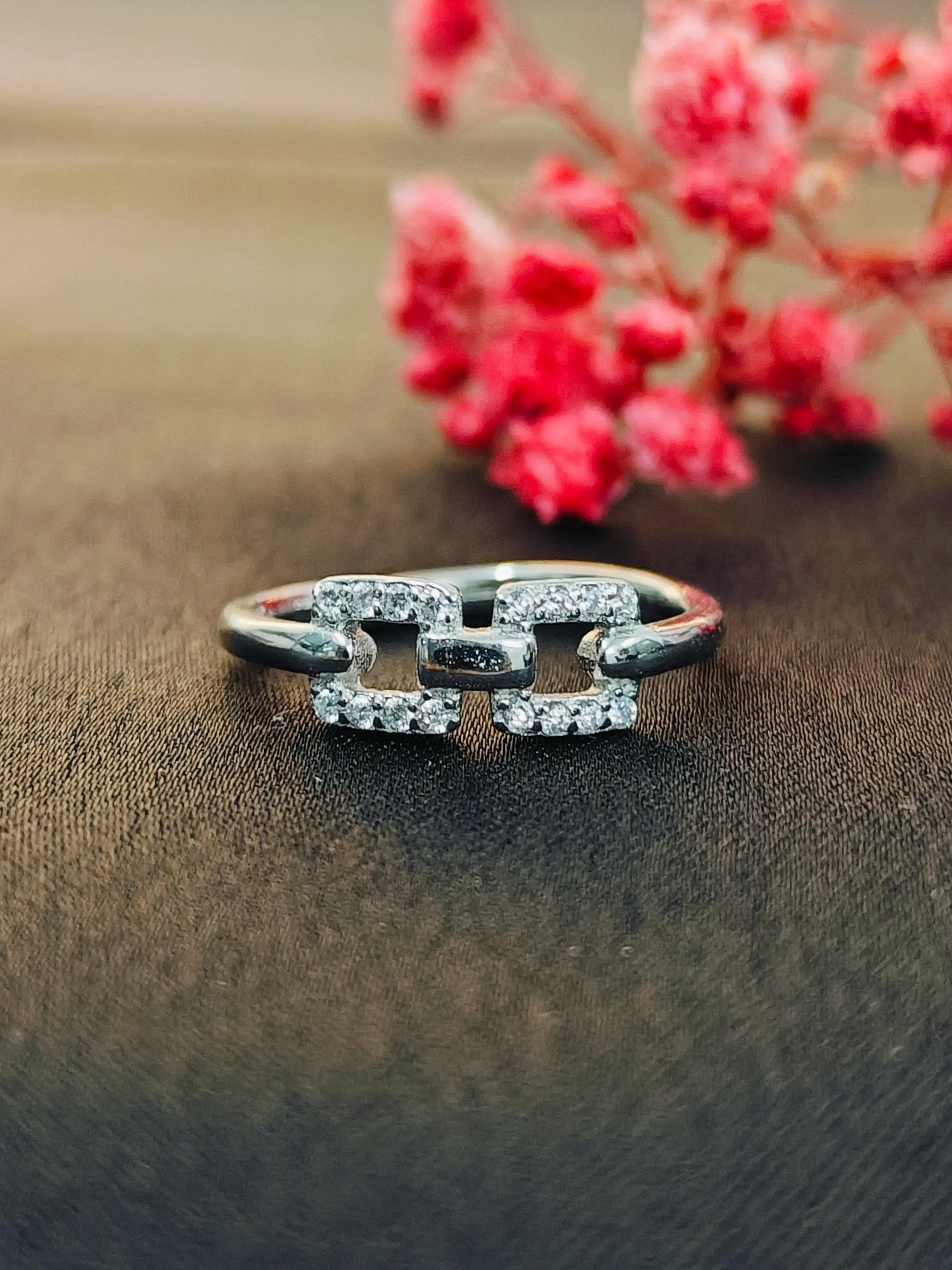 Silver ring with diamonds on a brown surface with red flowers in the background