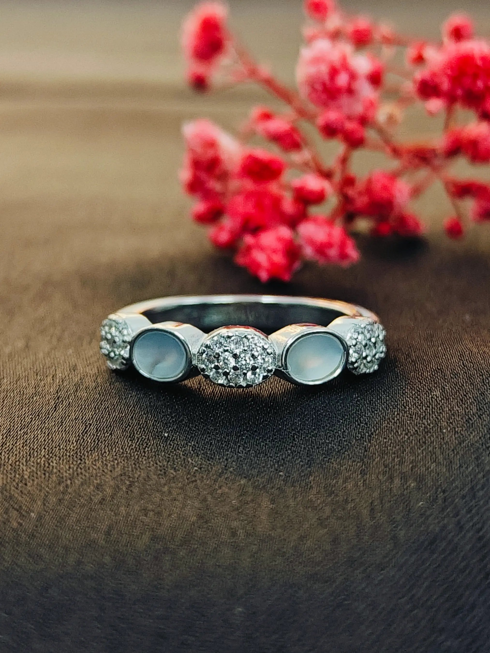 Silver ring with gemstones on a brown surface with red flowers in the background