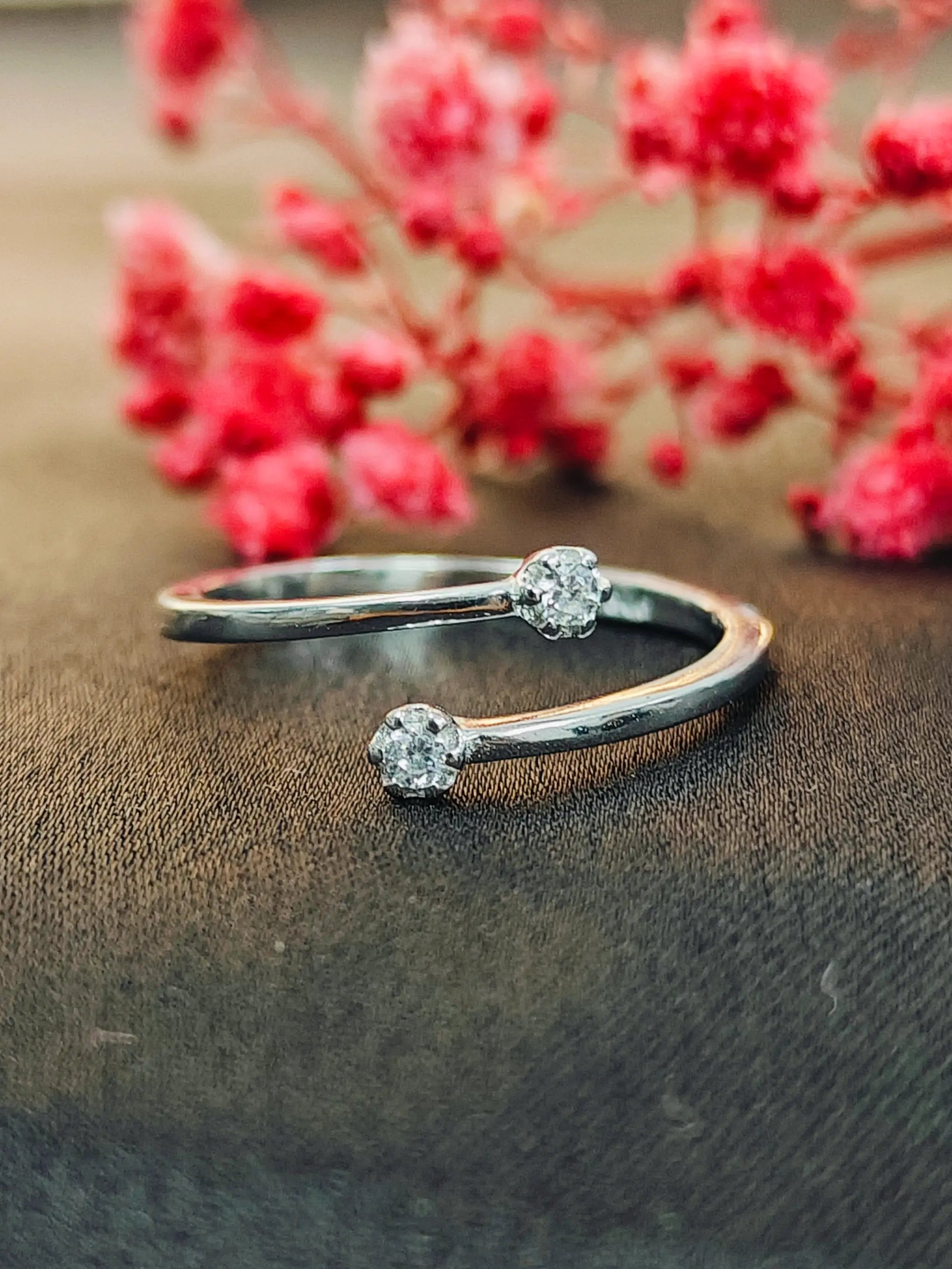 Silver open bangle with gemstones on a textured surface with red flowers in the background