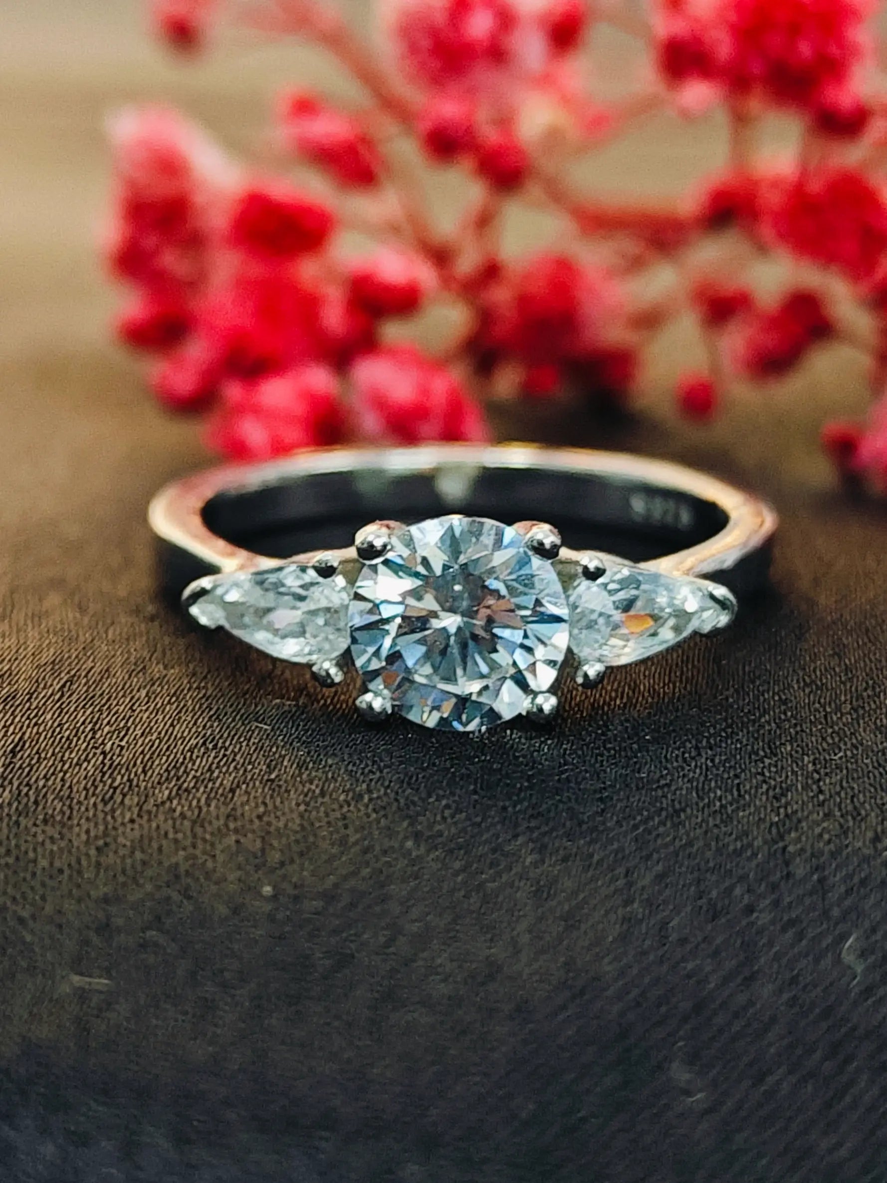 Diamond ring with floral design on a dark surface with red flowers in the background