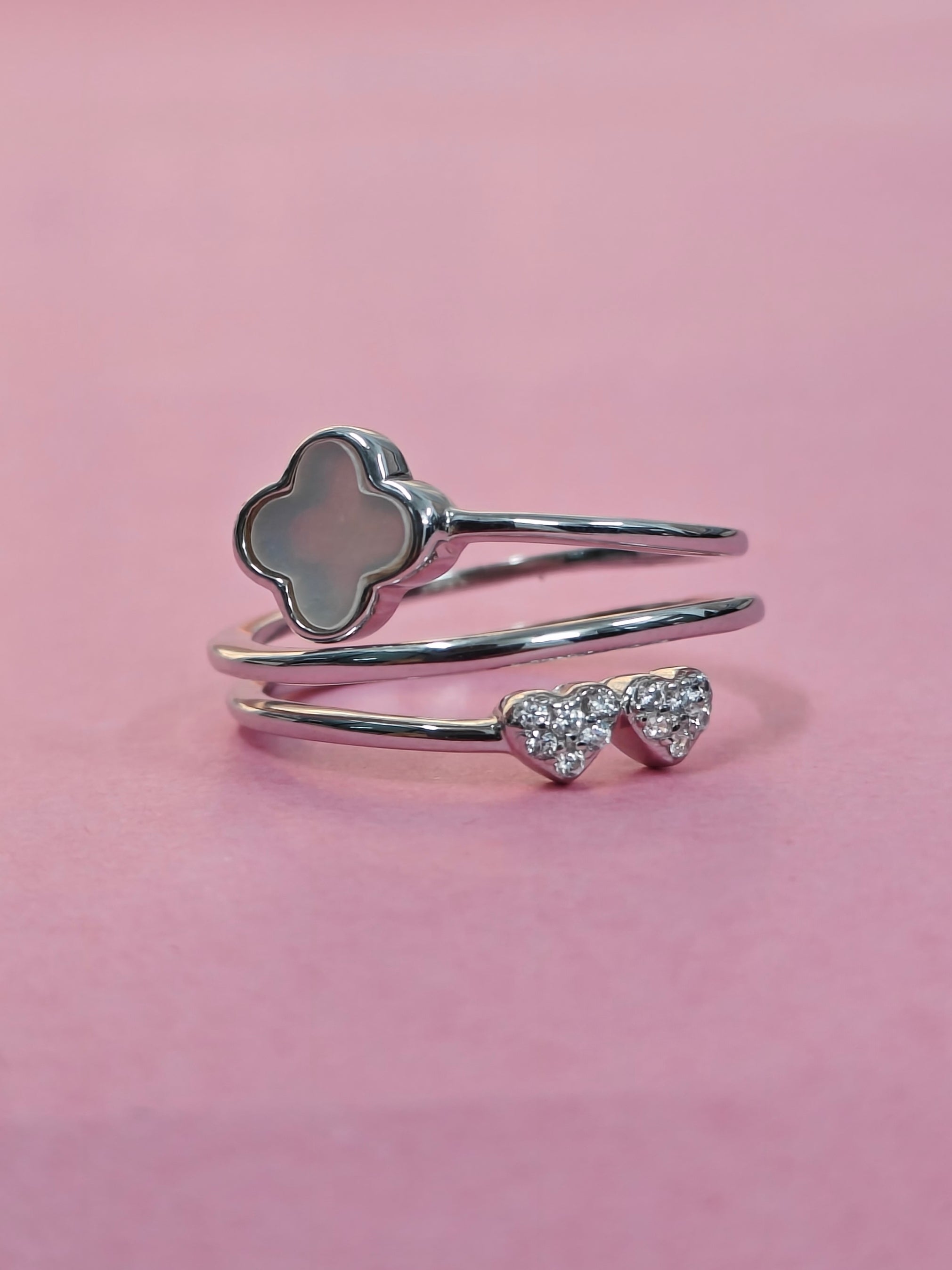 Silver ring with clover and heart designs on a pink background