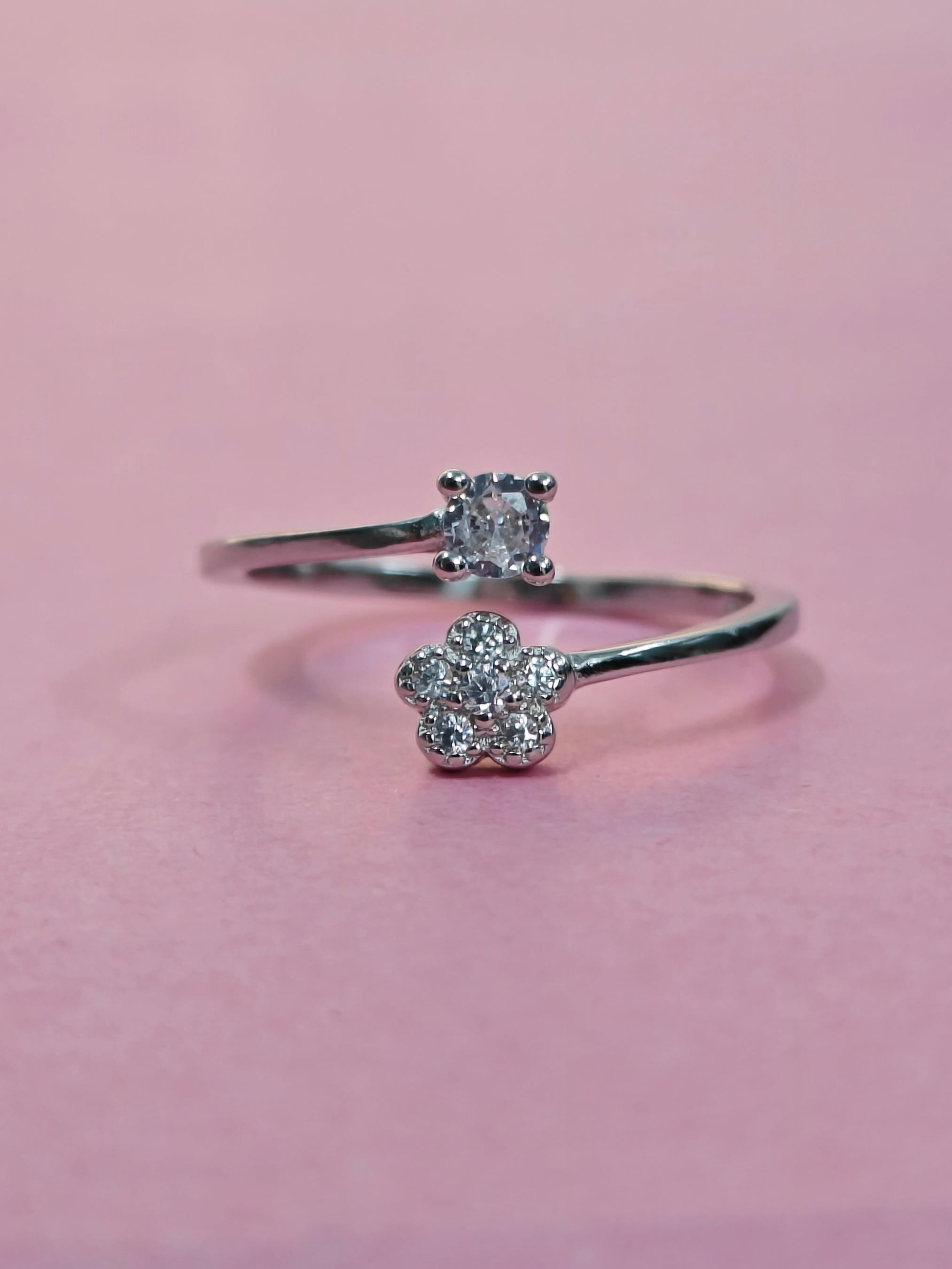 Silver ring with diamond flower design on a pink background