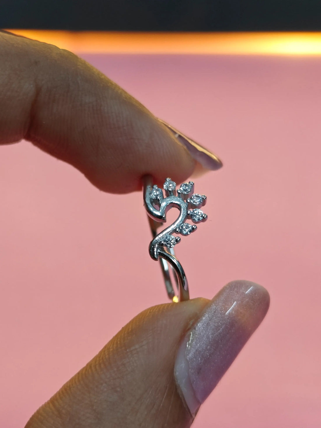 Silver ring with a unique design held by a hand against a pink background