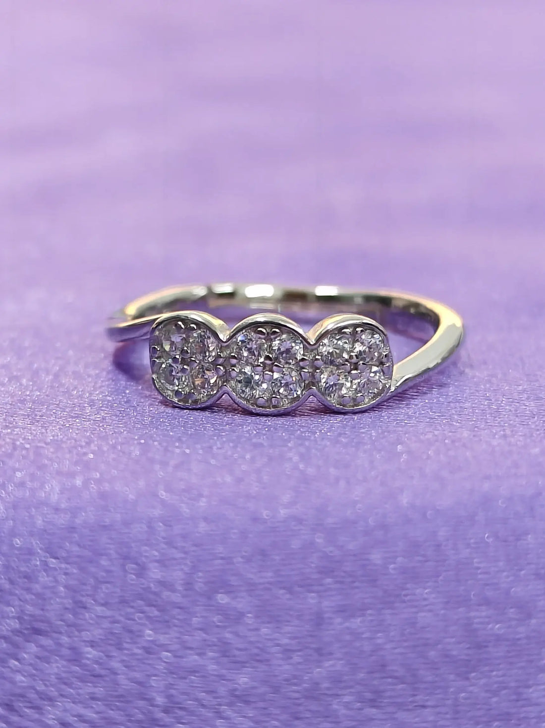 Silver ring with three circular gemstones on a purple background
