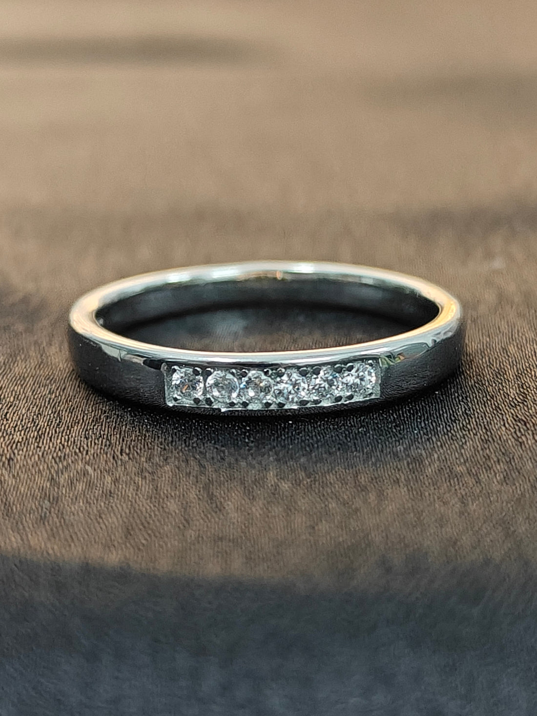 Silver ring with embedded diamonds on a brown fabric background