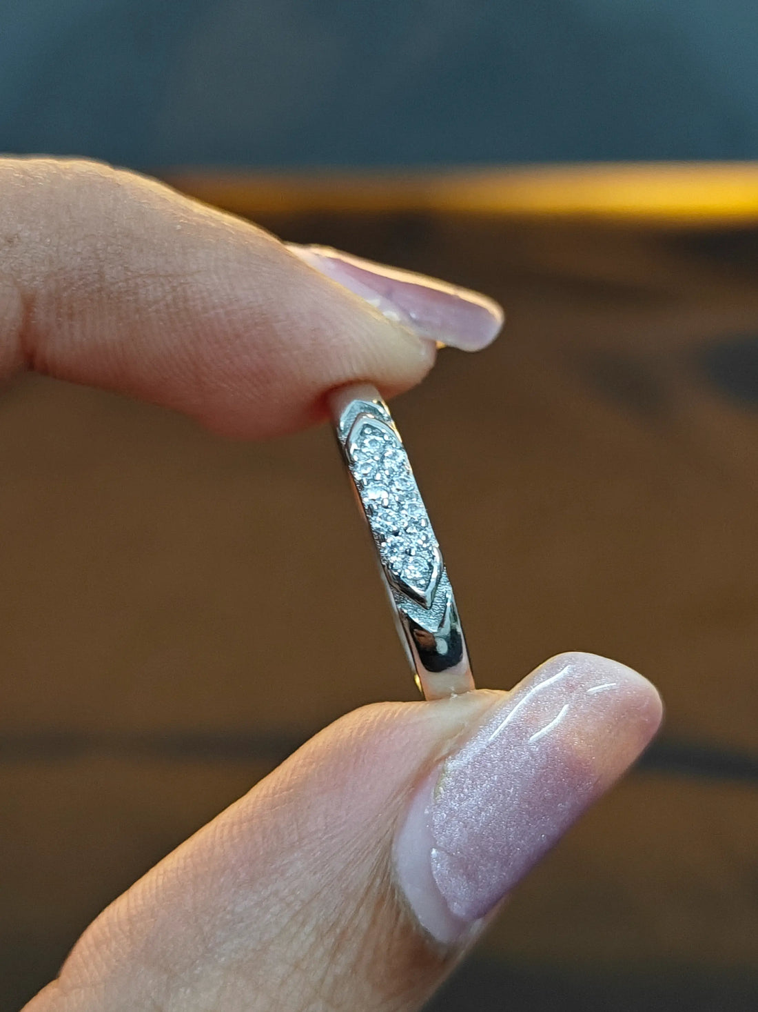 Silver ring with diamonds held between fingers against a blurred background