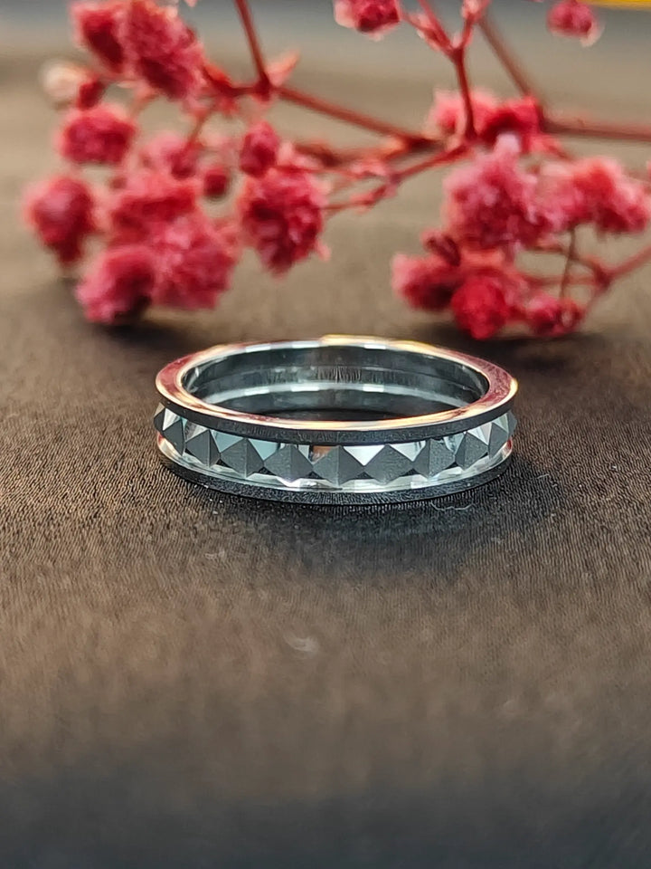 Silver ring with geometric pattern on a brown surface with pink flowers in the background