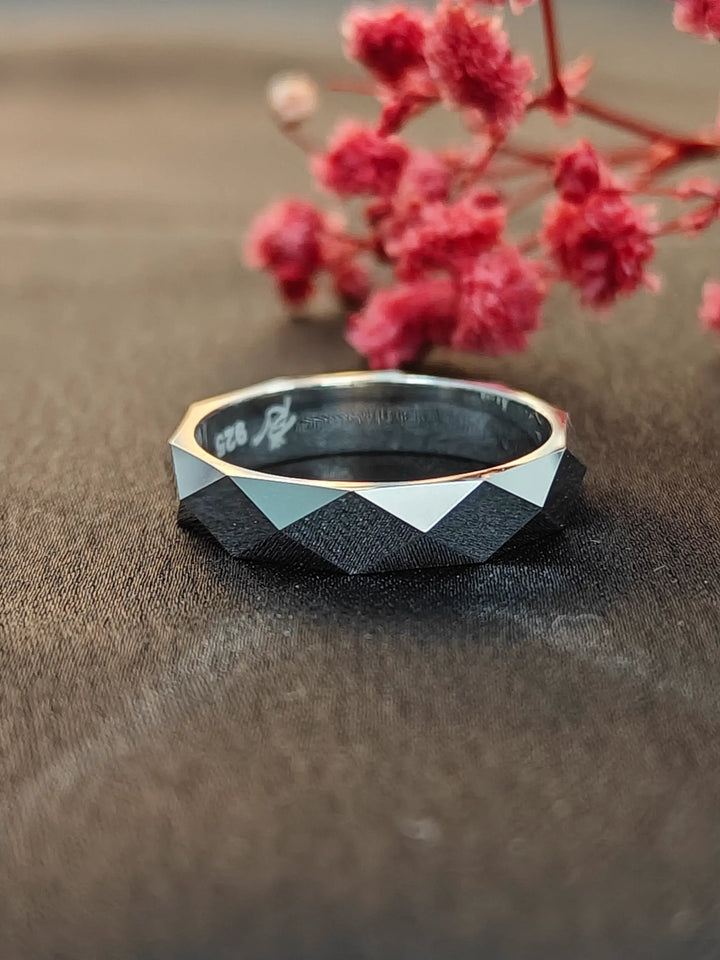 Black geometric ring with gold accents on a brown surface with pink flowers.