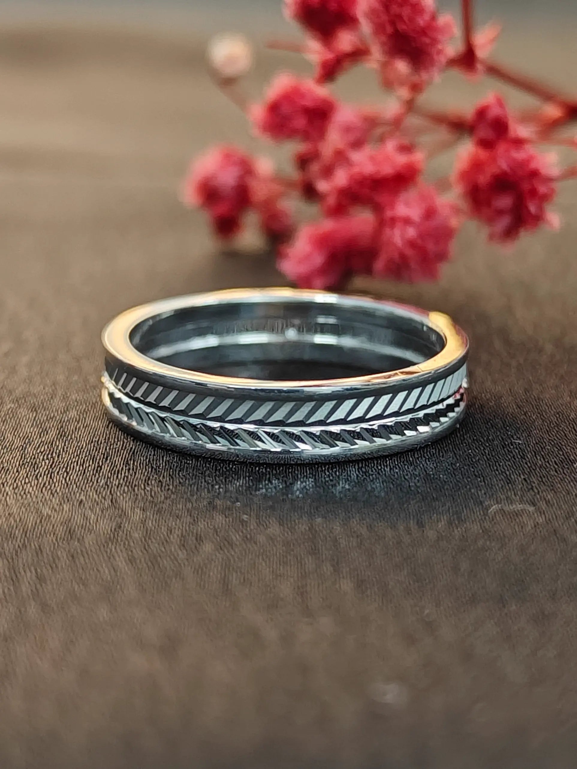 Silver ring with intricate design on a brown surface with pink flowers in the background