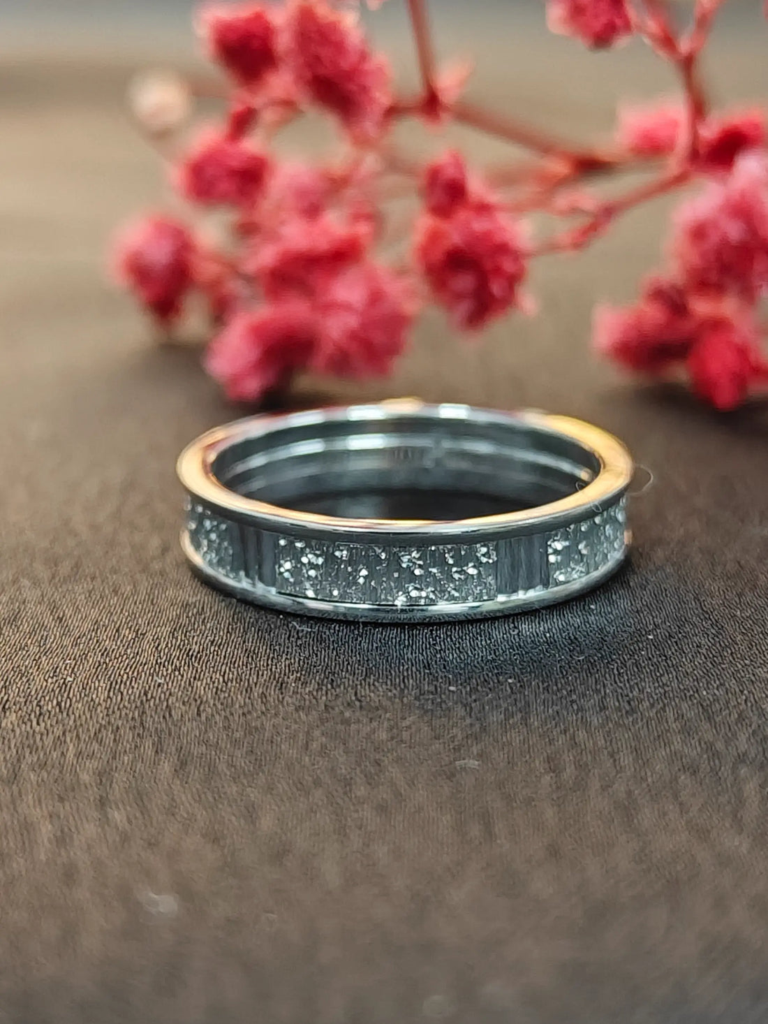 Silver ring with star pattern on a textured surface with pink flowers in the background