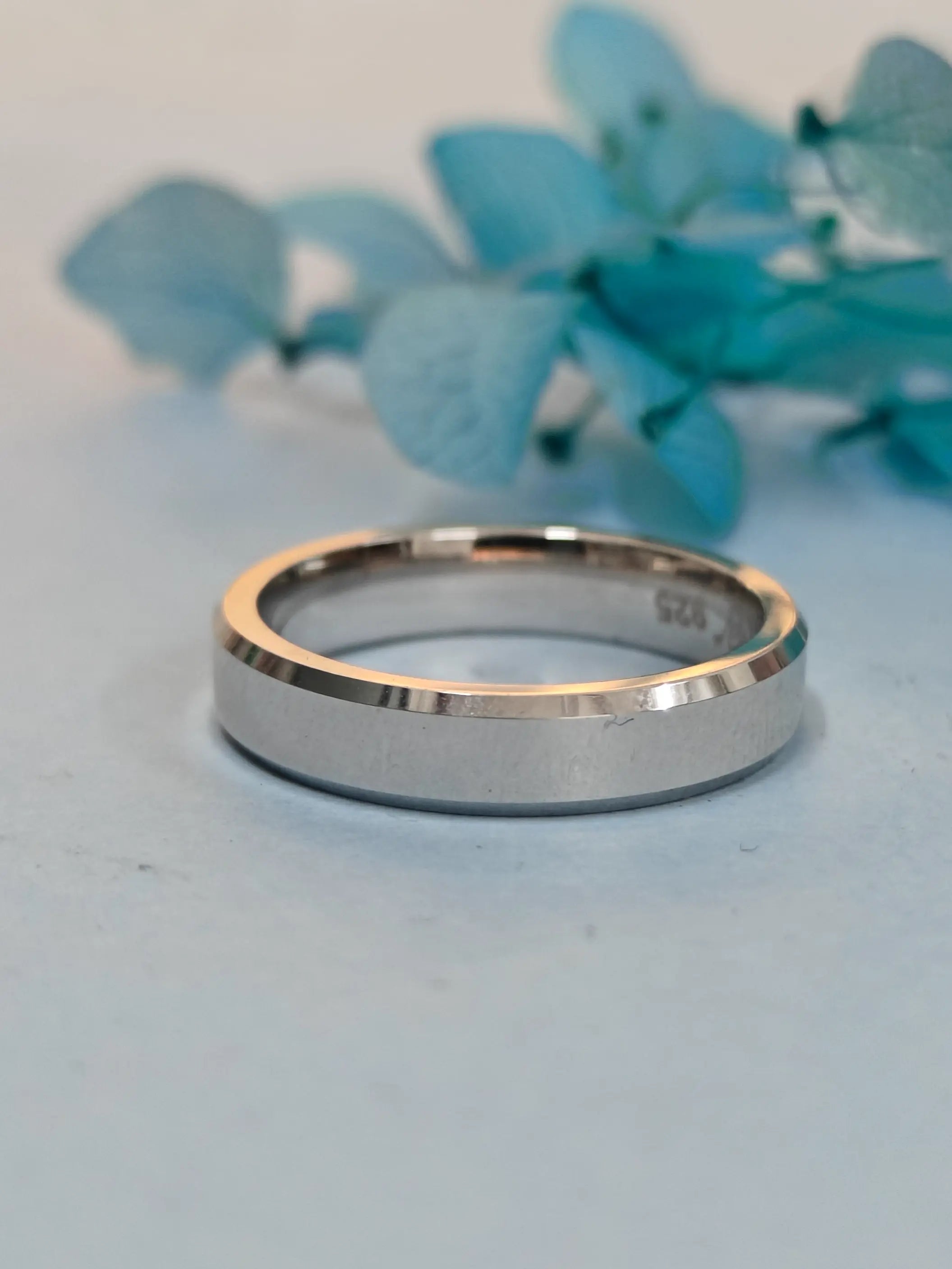 Silver ring with rose gold accent on a light blue background with floral elements