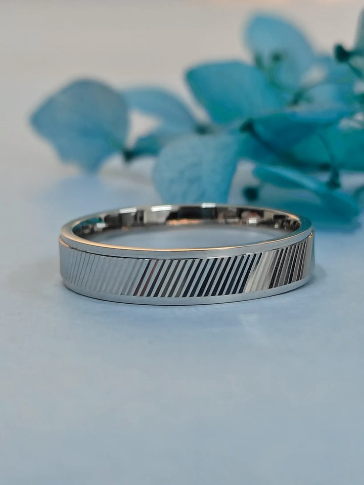 Silver ring with a textured band on a light blue background with blue flowers.