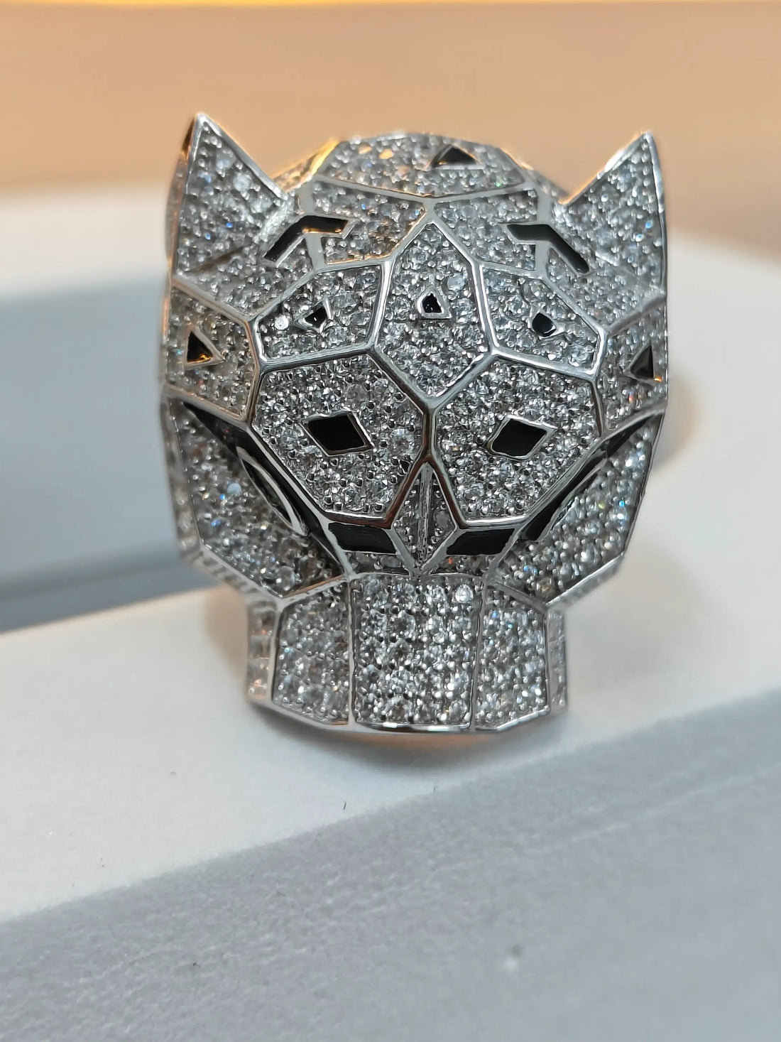 Silver panther head pendant on a white surface with a blurred background