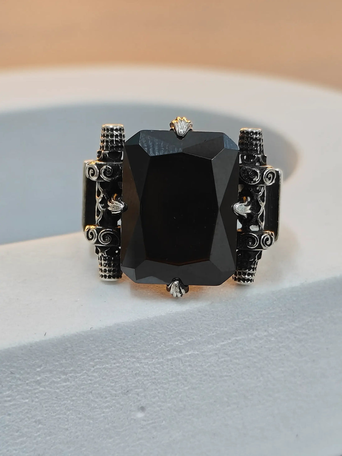 Black gemstone ring with intricate silver designs on a light gray surface