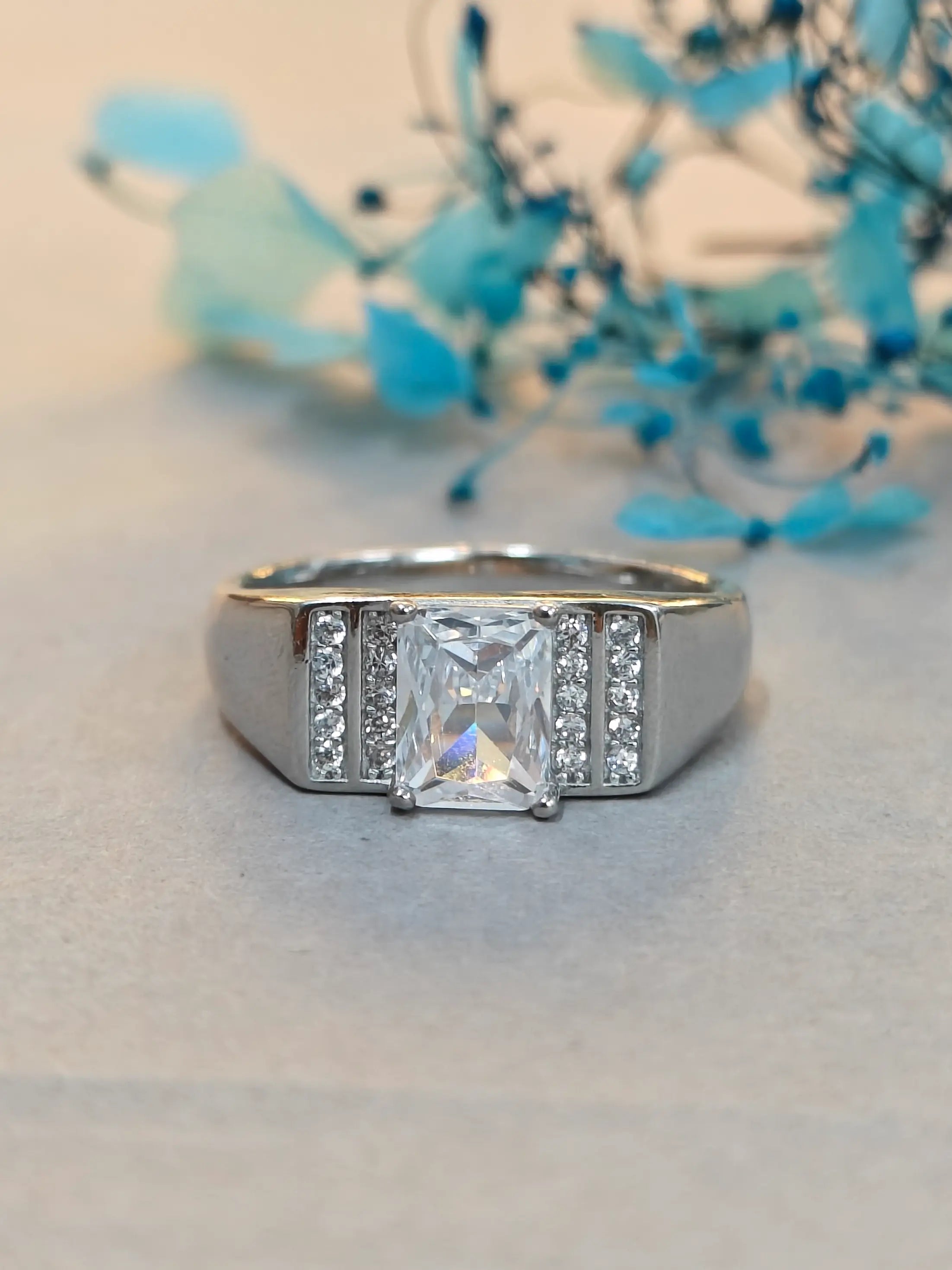 Silver ring with a large diamond and smaller diamonds on the band, placed on a light surface with blue decorative elements.