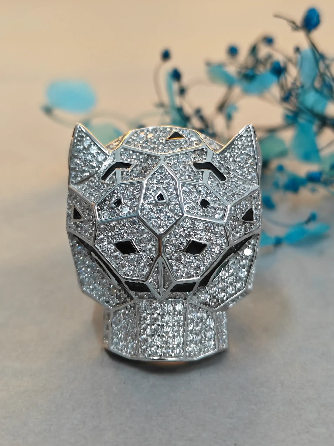 Silver panther head-shaped object with gemstones on a light background