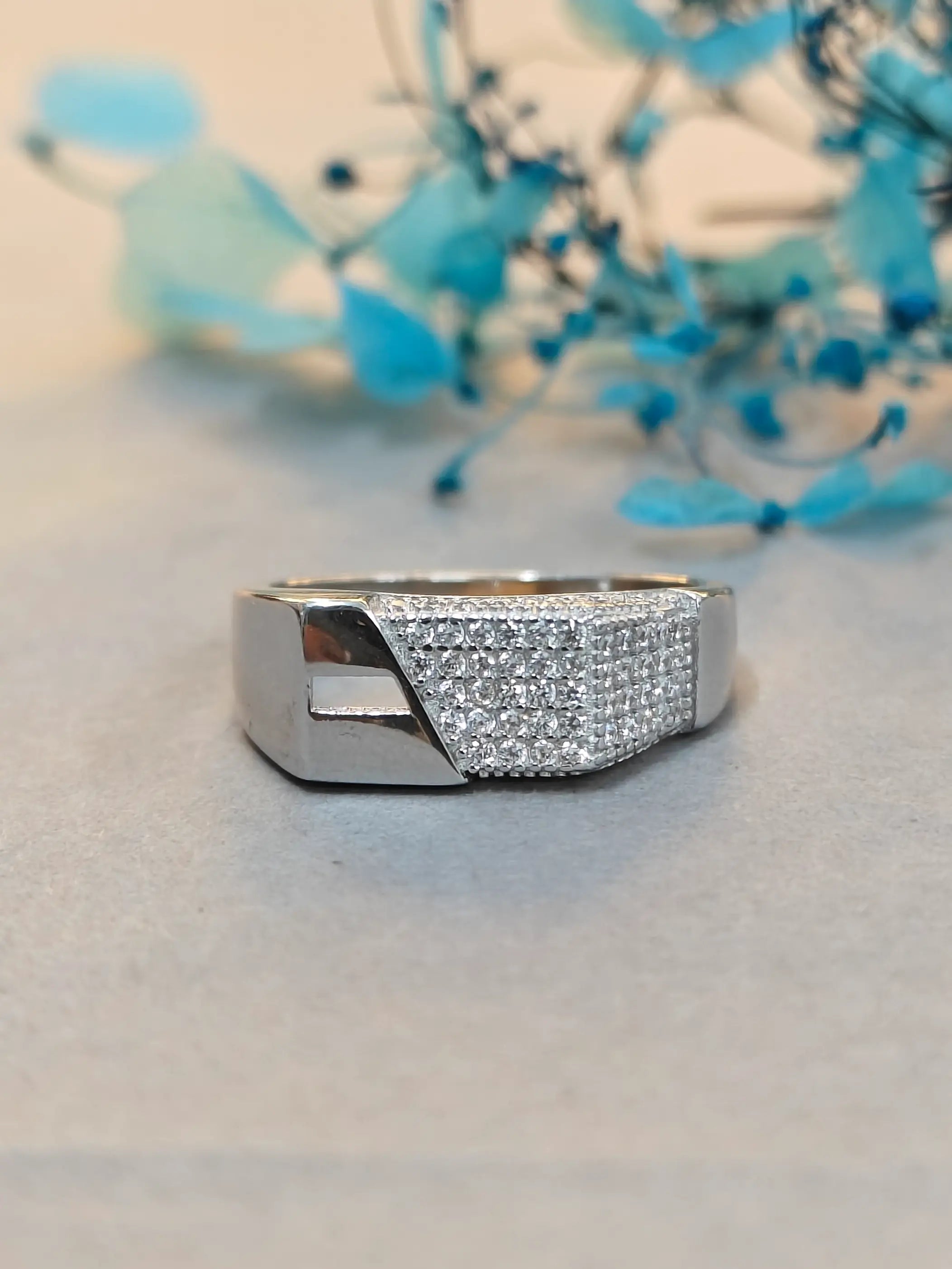 Silver ring with diamond accents on a light gray surface with blue decorative elements in the background