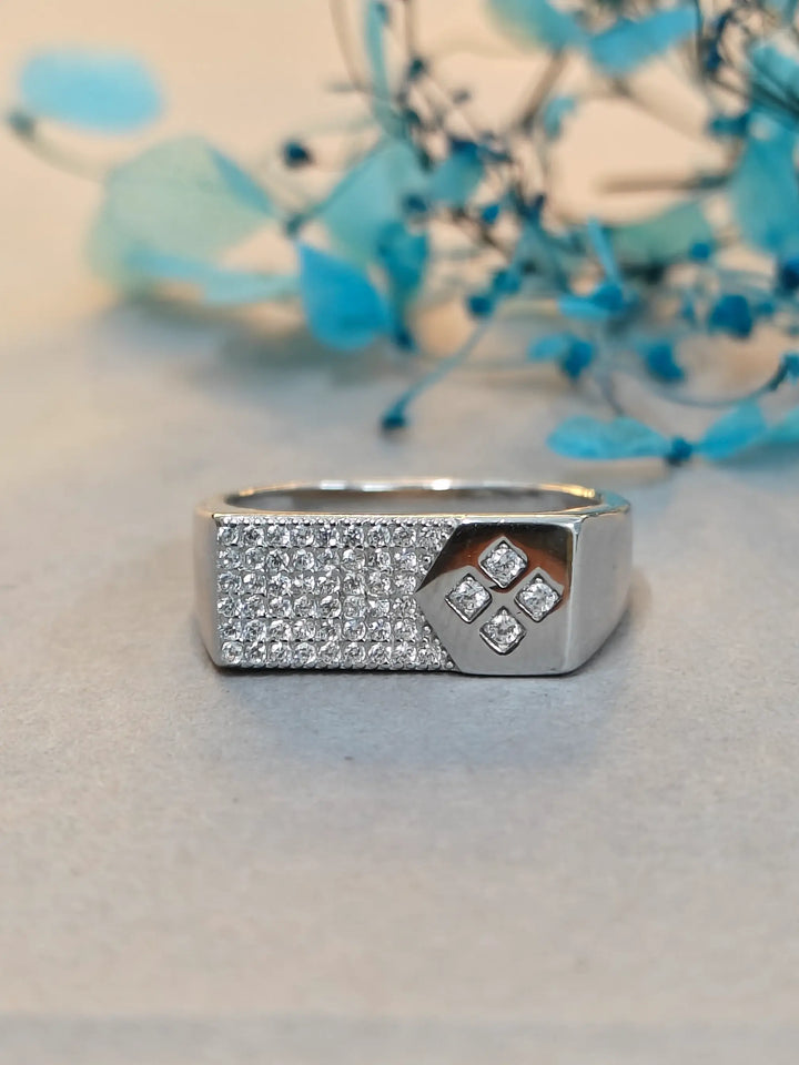 Silver ring with diamond accents on a light surface with blurred floral background