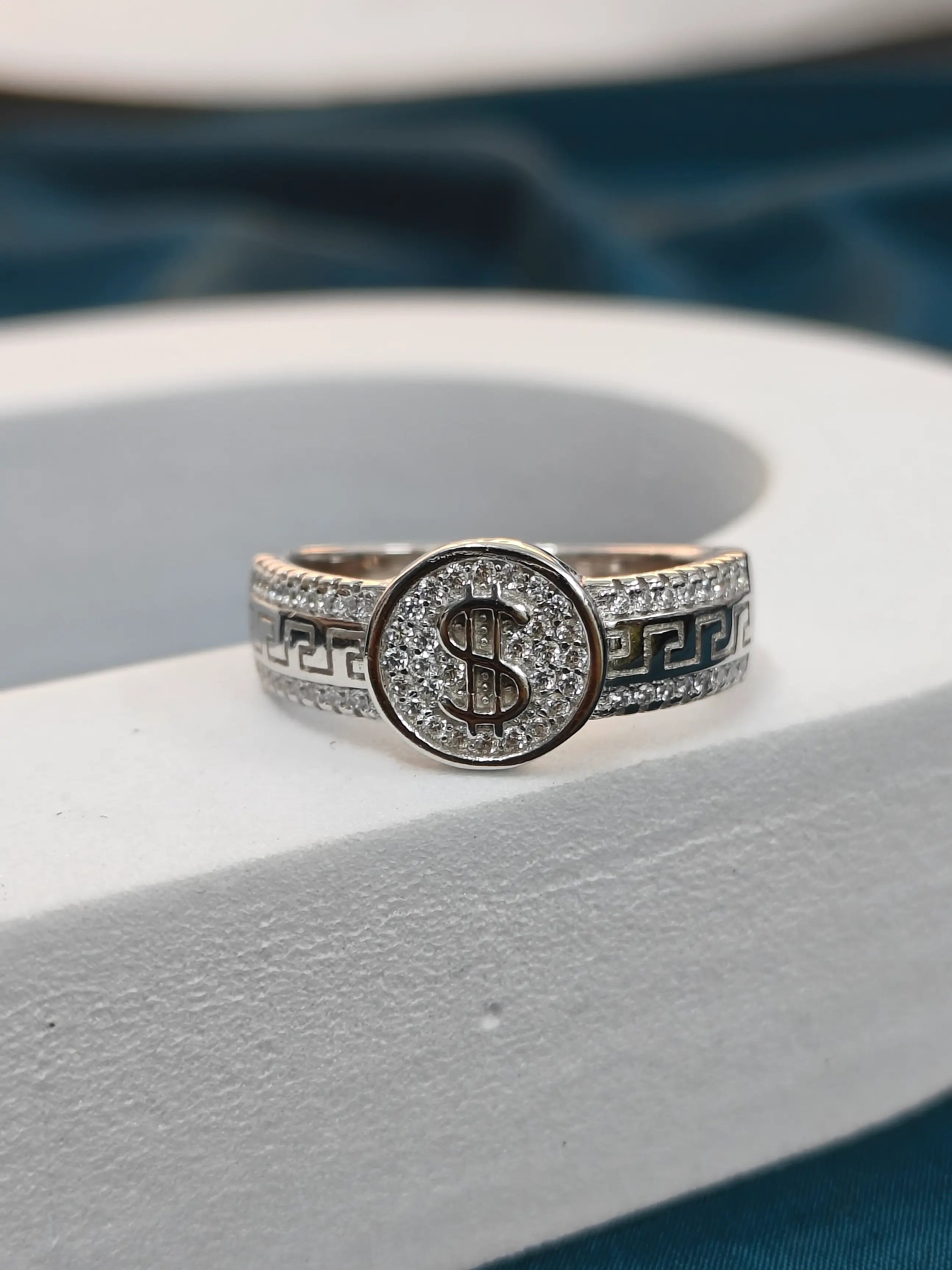 Silver ring with a dollar sign design on a white surface