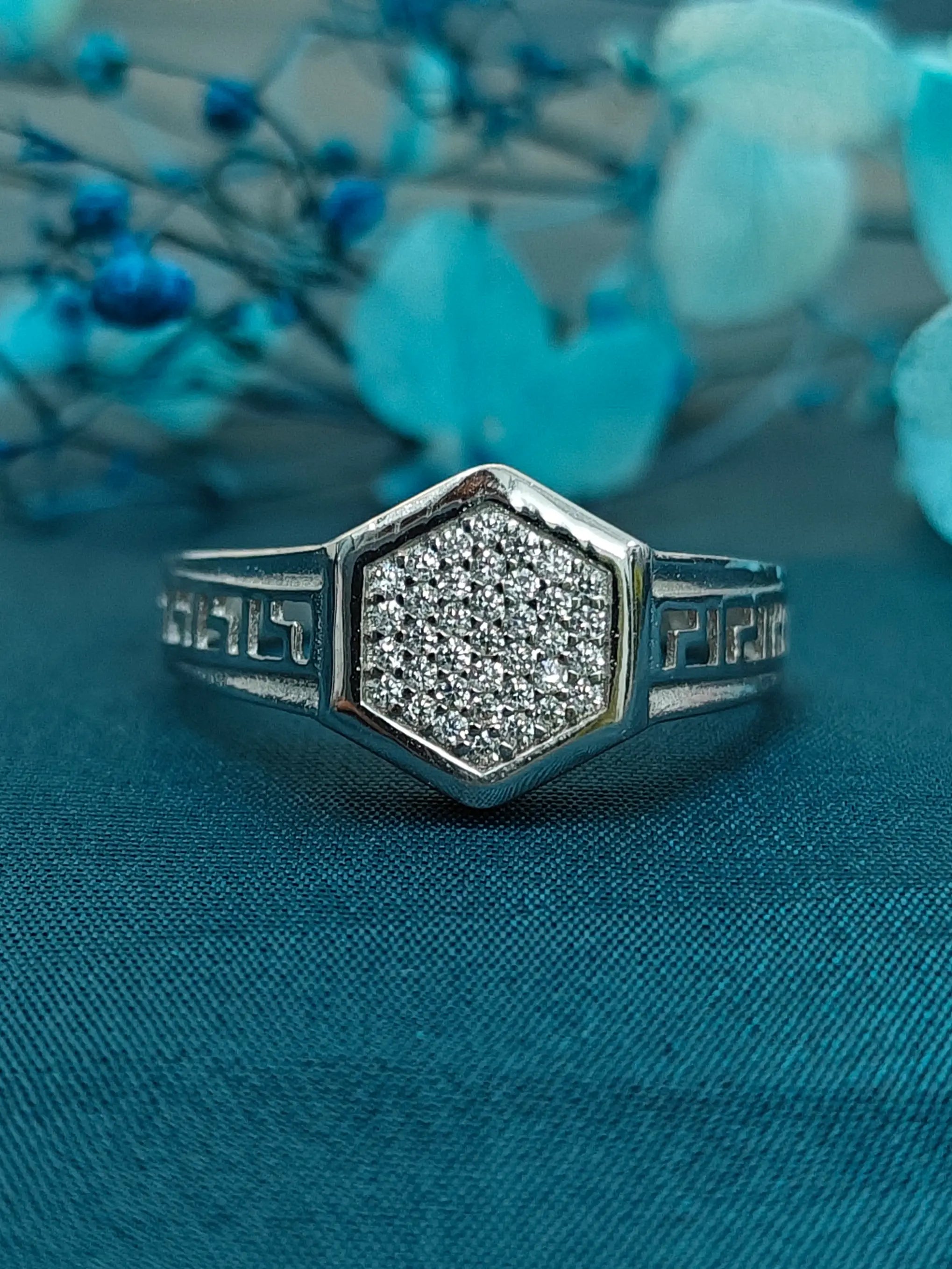 Silver ring with hexagonal diamond design on a blue fabric background