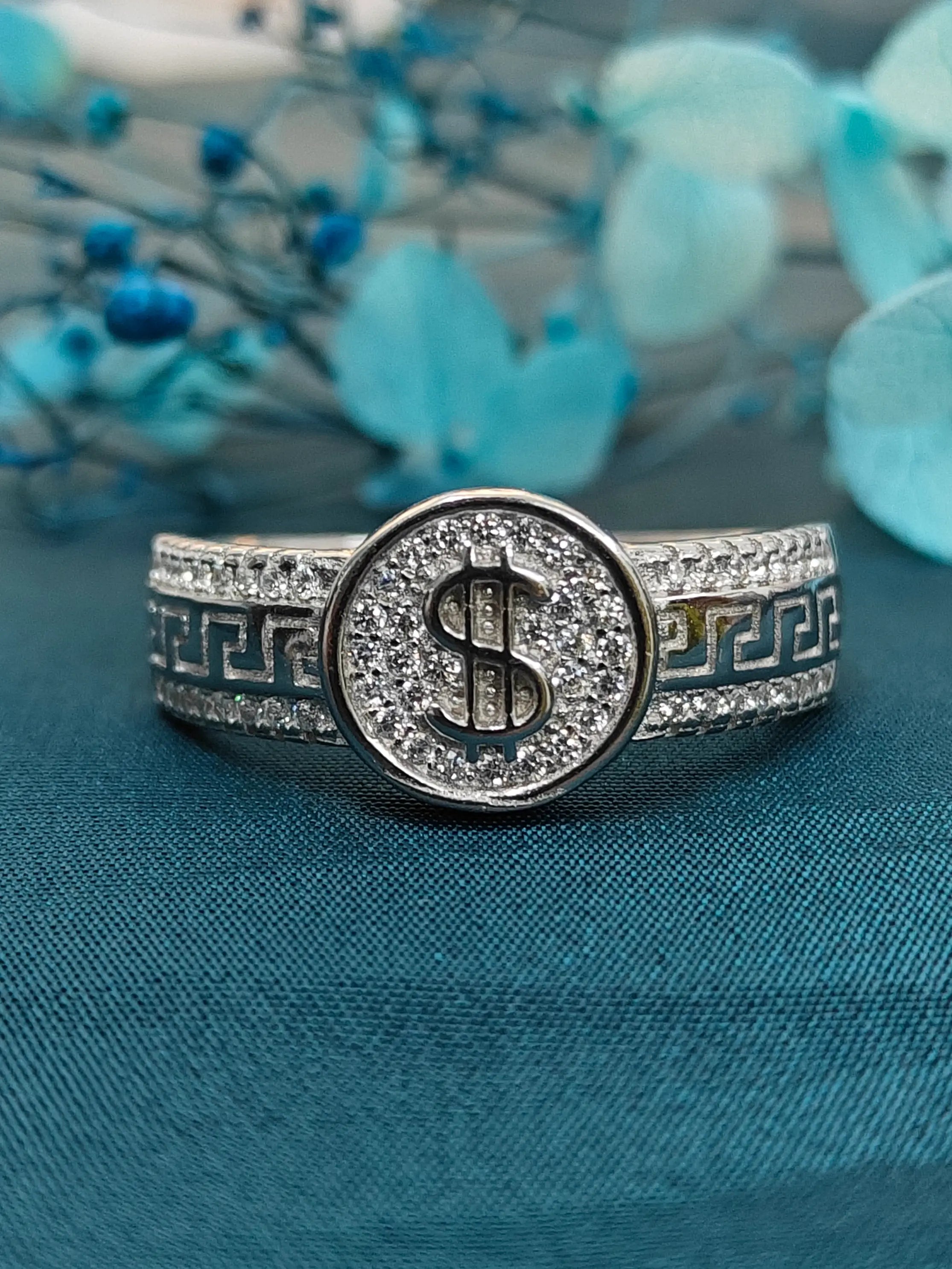 Silver ring with a dollar sign design on a blue fabric background