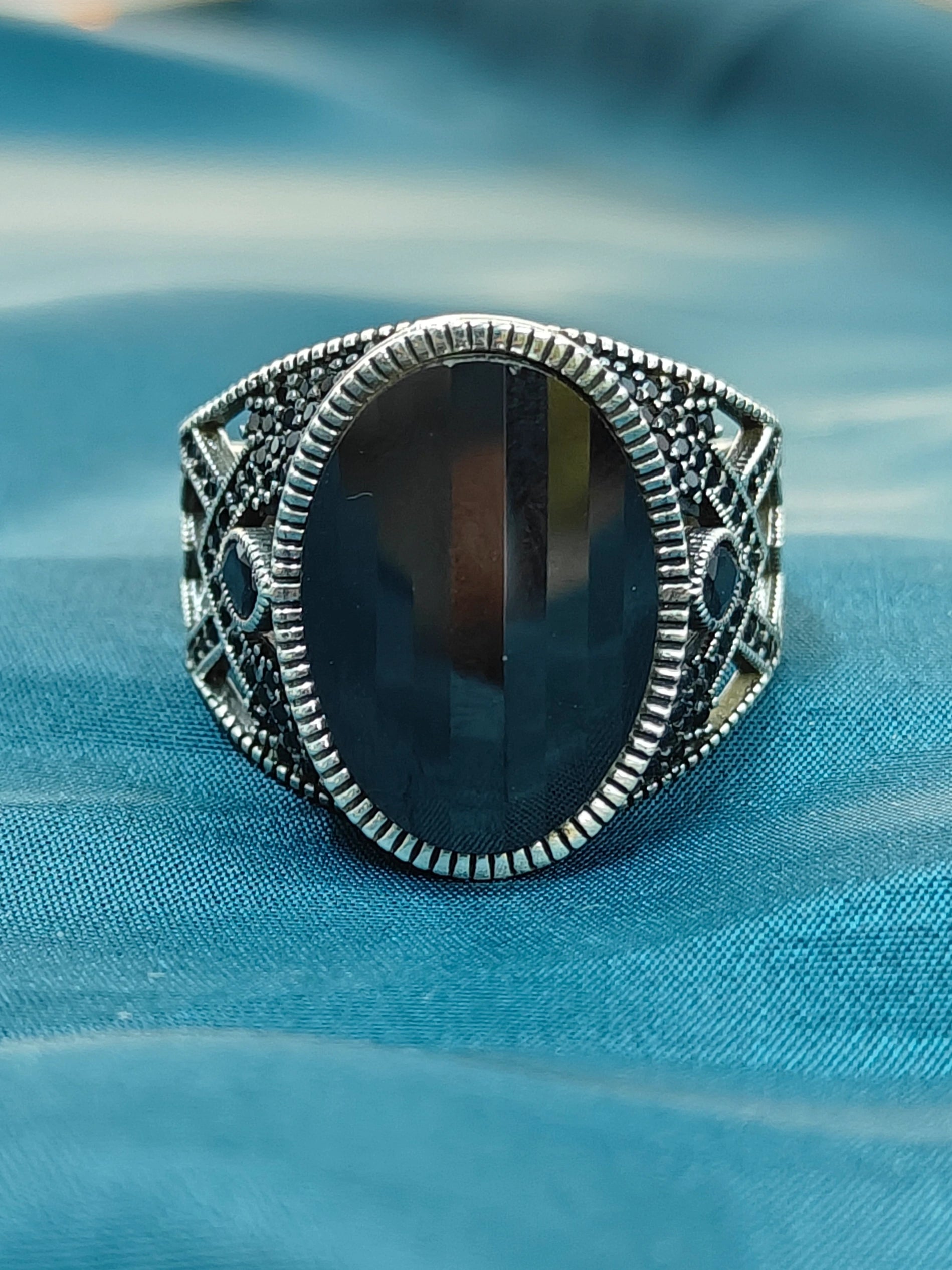 Silver ring with a large black stone on a blue fabric background