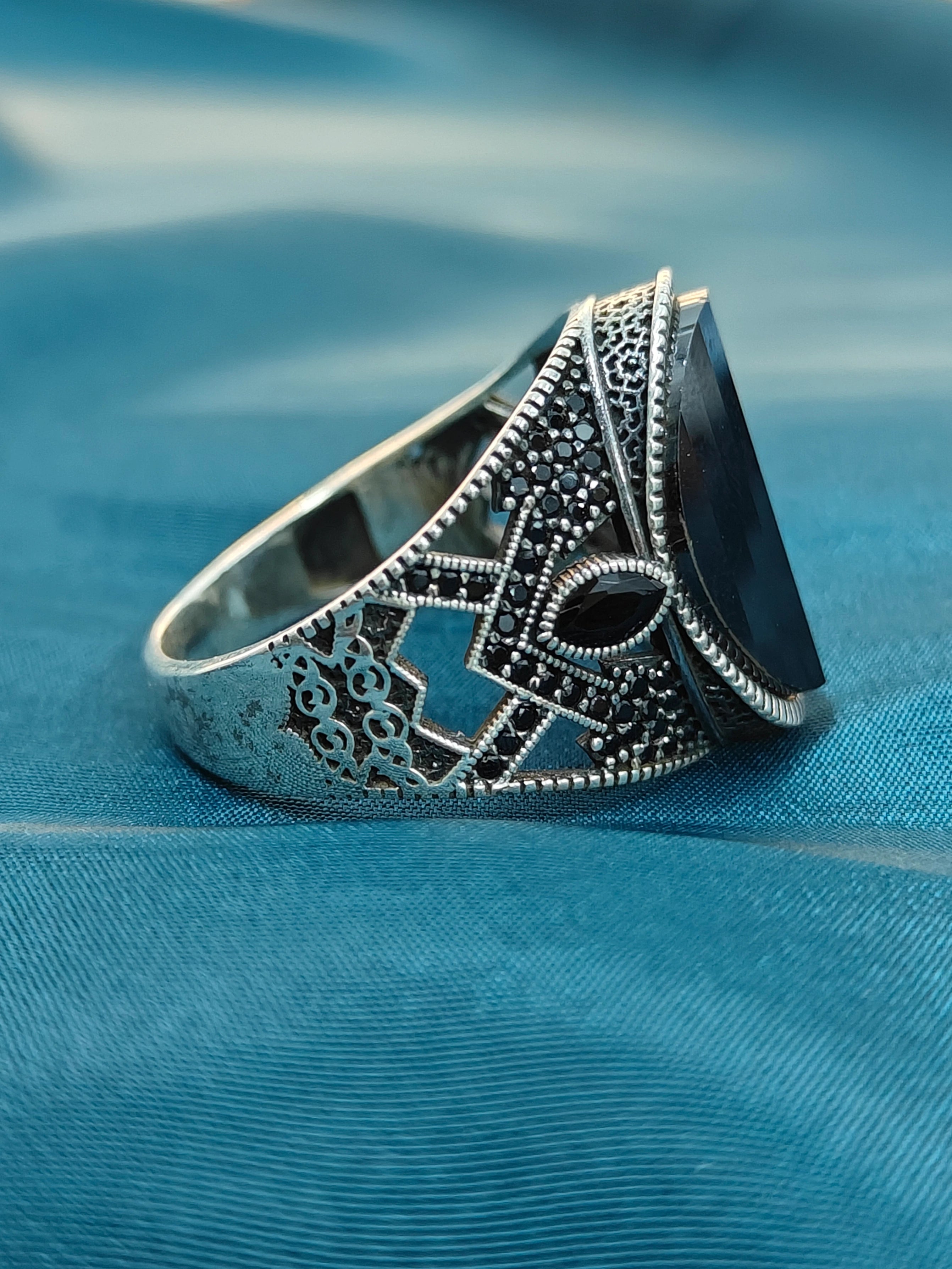 Silver ring with intricate design on a blue fabric background