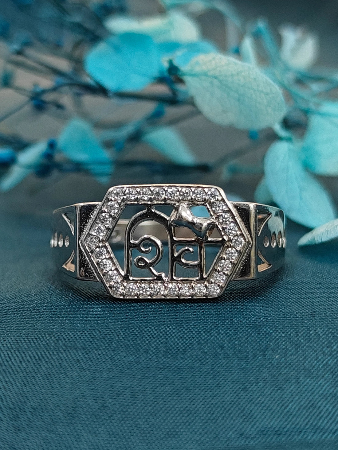 Silver ring with decorative design on a blue fabric background