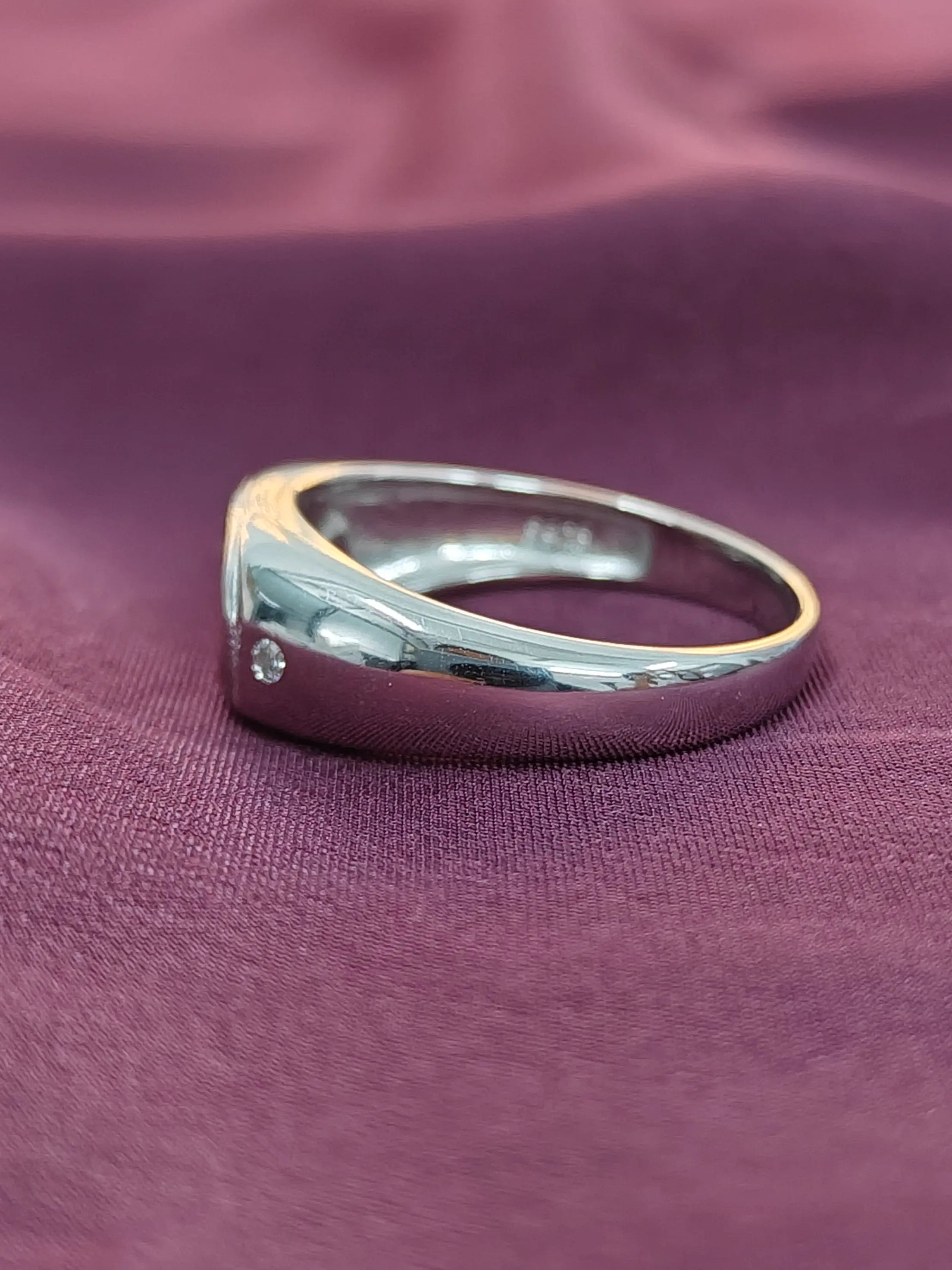 Silver ring with a small diamond on a purple fabric background