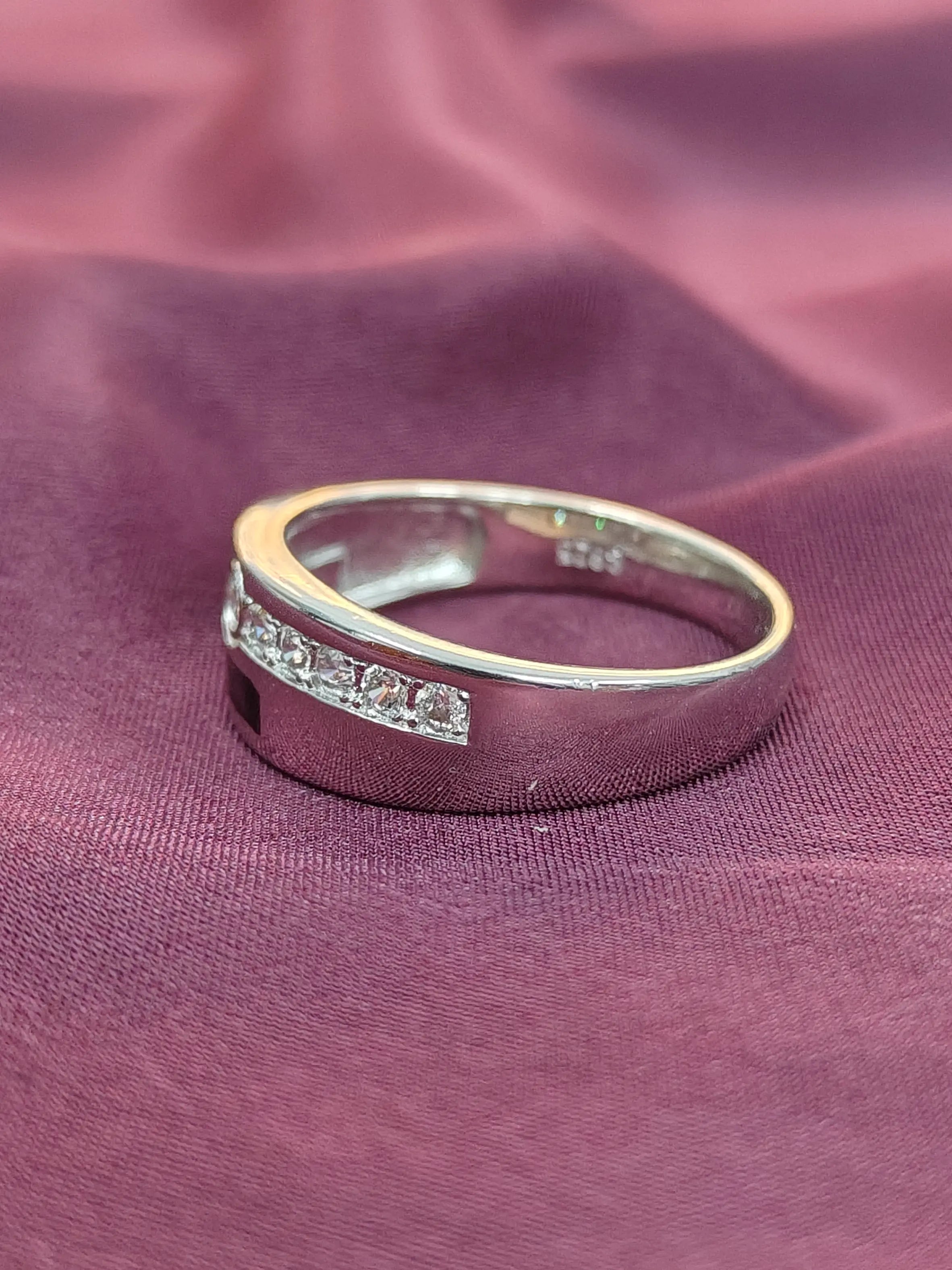 Silver ring with small diamonds on a purple fabric background.