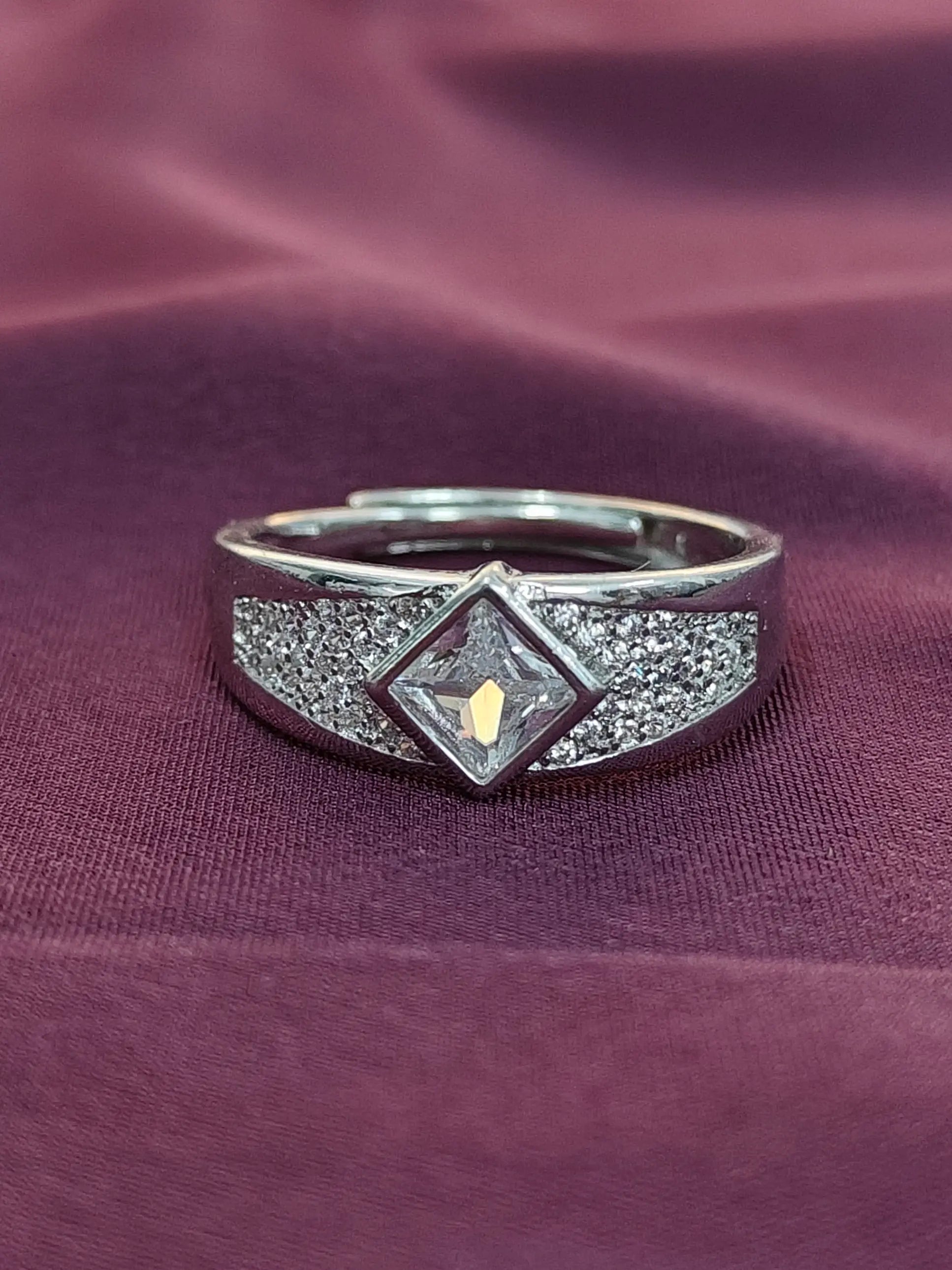 Silver ring with a diamond-shaped center and gold accent on a purple fabric background