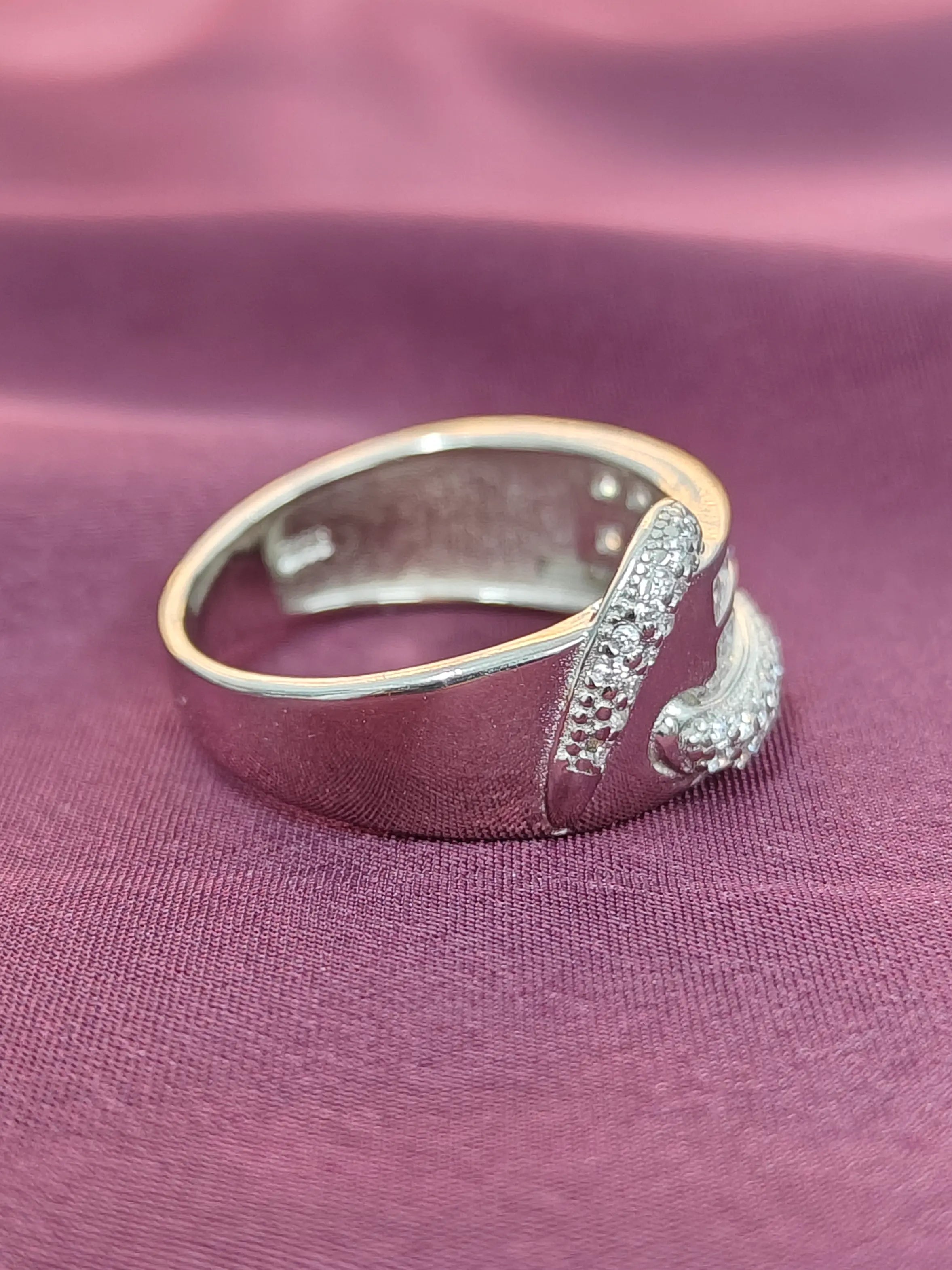 Silver ring with a decorative design on a purple fabric background